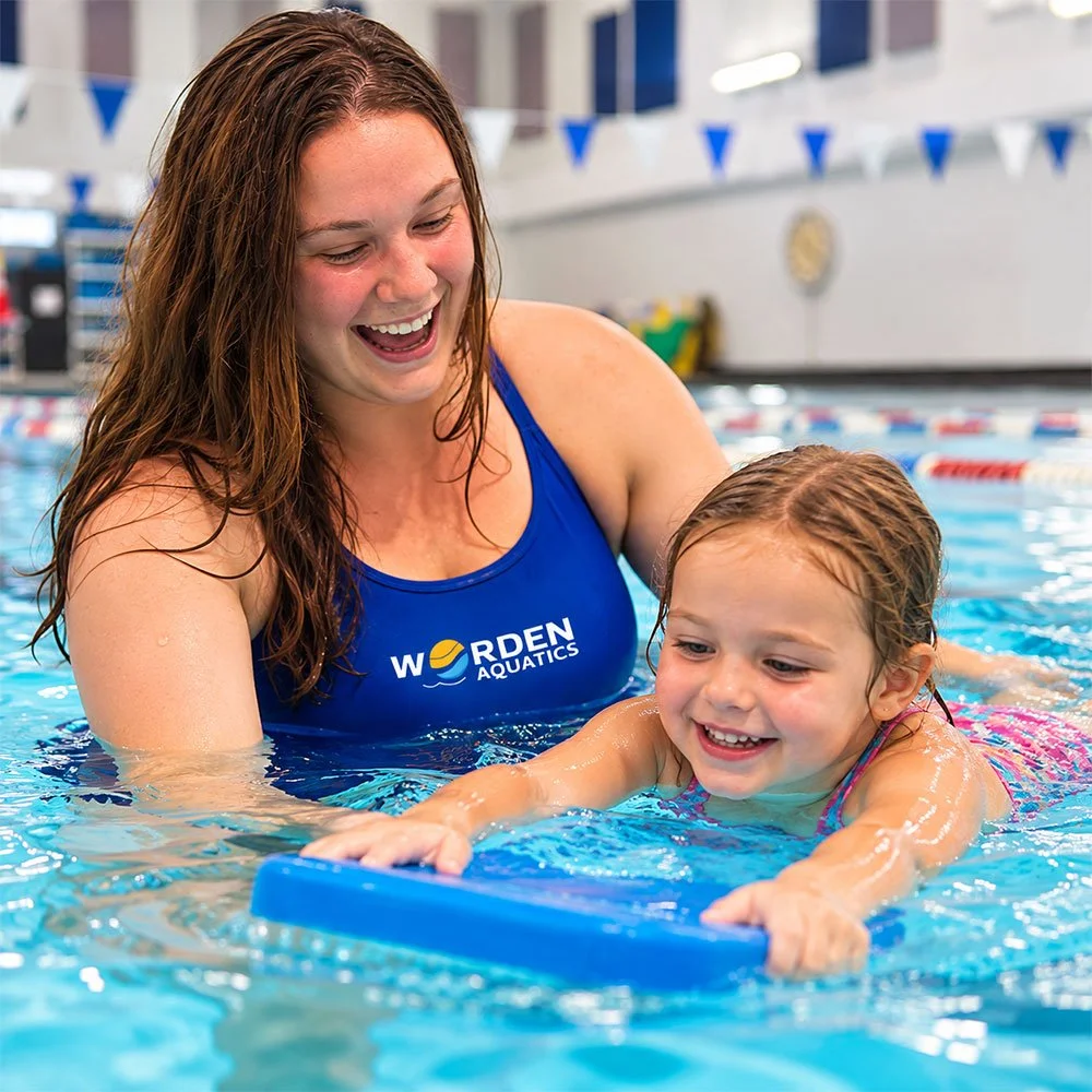 Coach Fiona of Worden Aquatics smiles as she helps a young girl practice swimming with a kickboard during a private swim lesson in Nashville, TN.