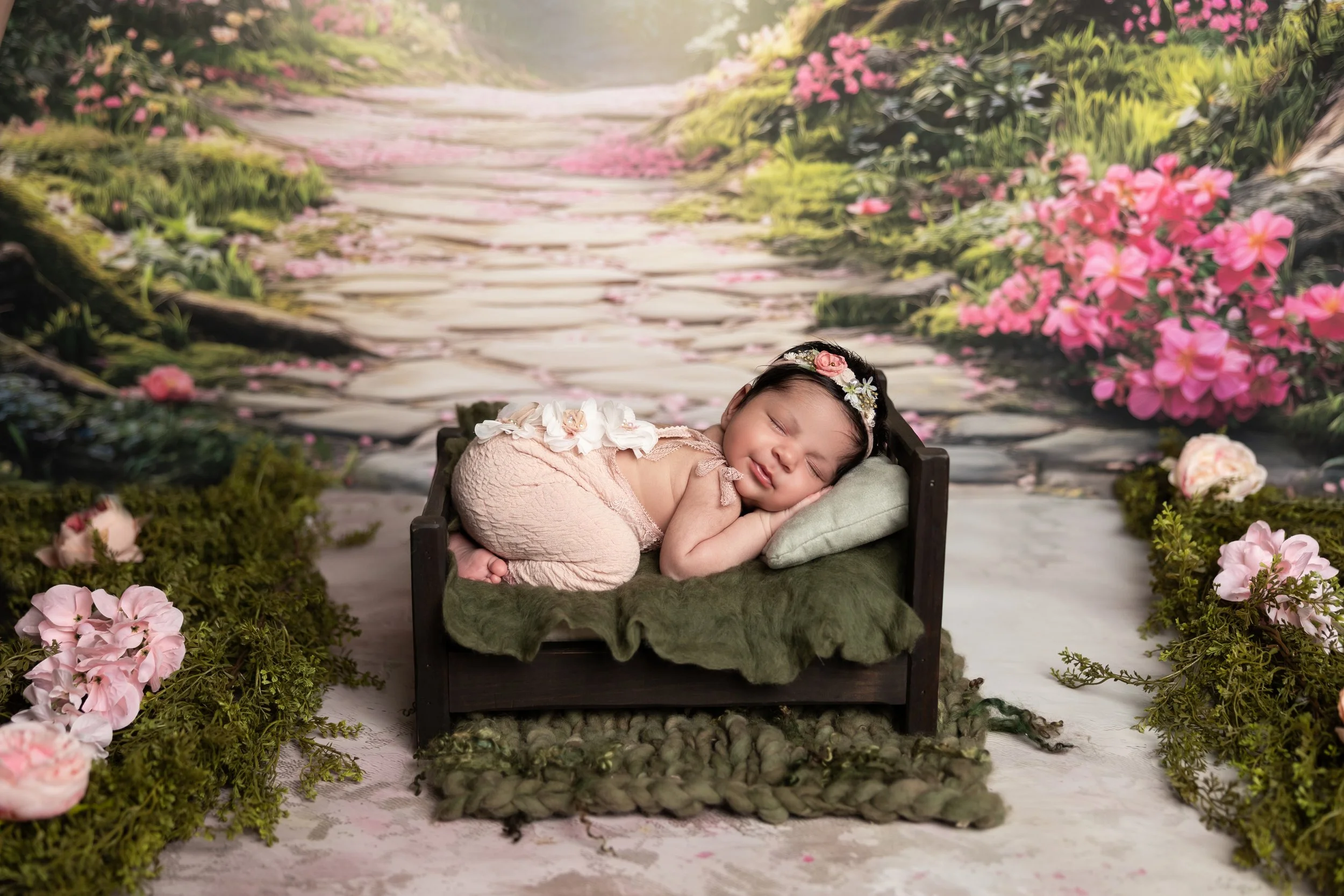 Storybook-inspired newborn photography featuring a sleeping baby posed on a miniature bed surrounded by florals and whimsical styling.