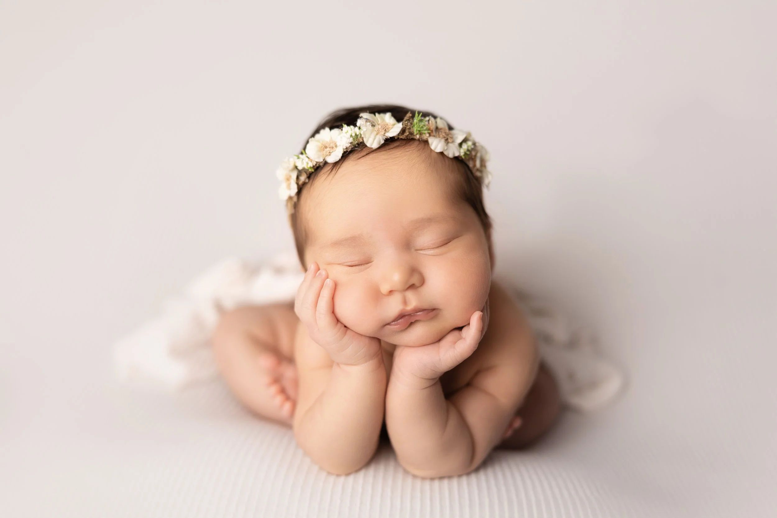Sleeping newborn baby posed with chin resting on hands and wearing a delicate floral crown during a baby-only newborn photography session by Austin newborn photographer Jessica Doffing.