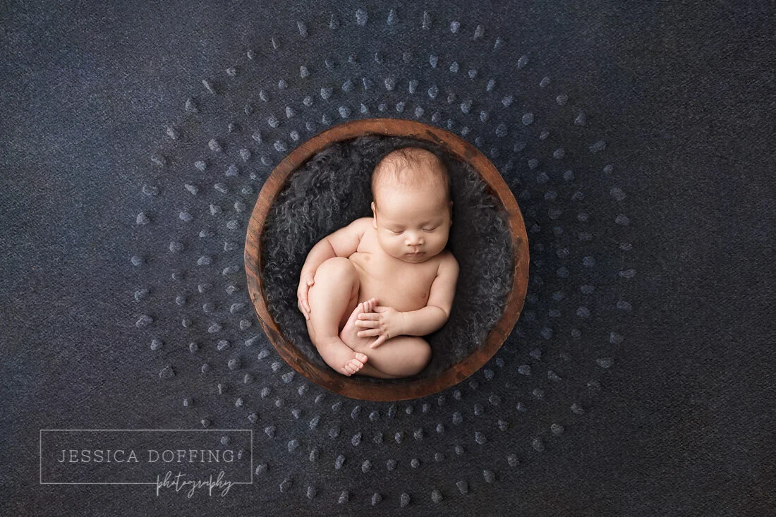 Sleeping newborn baby posed in a wooden bowl on a textured dark backdrop during an Austin newborn photography session.