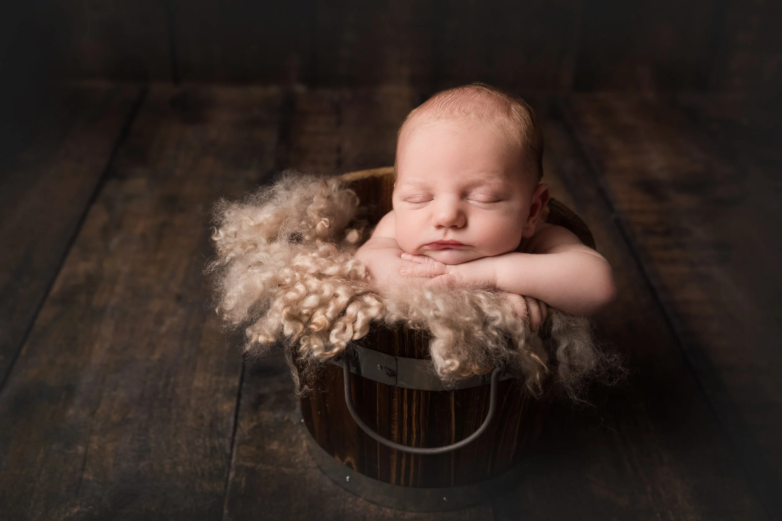 Sleeping newborn baby in a wooden bucket during an Austin newborn photography session.