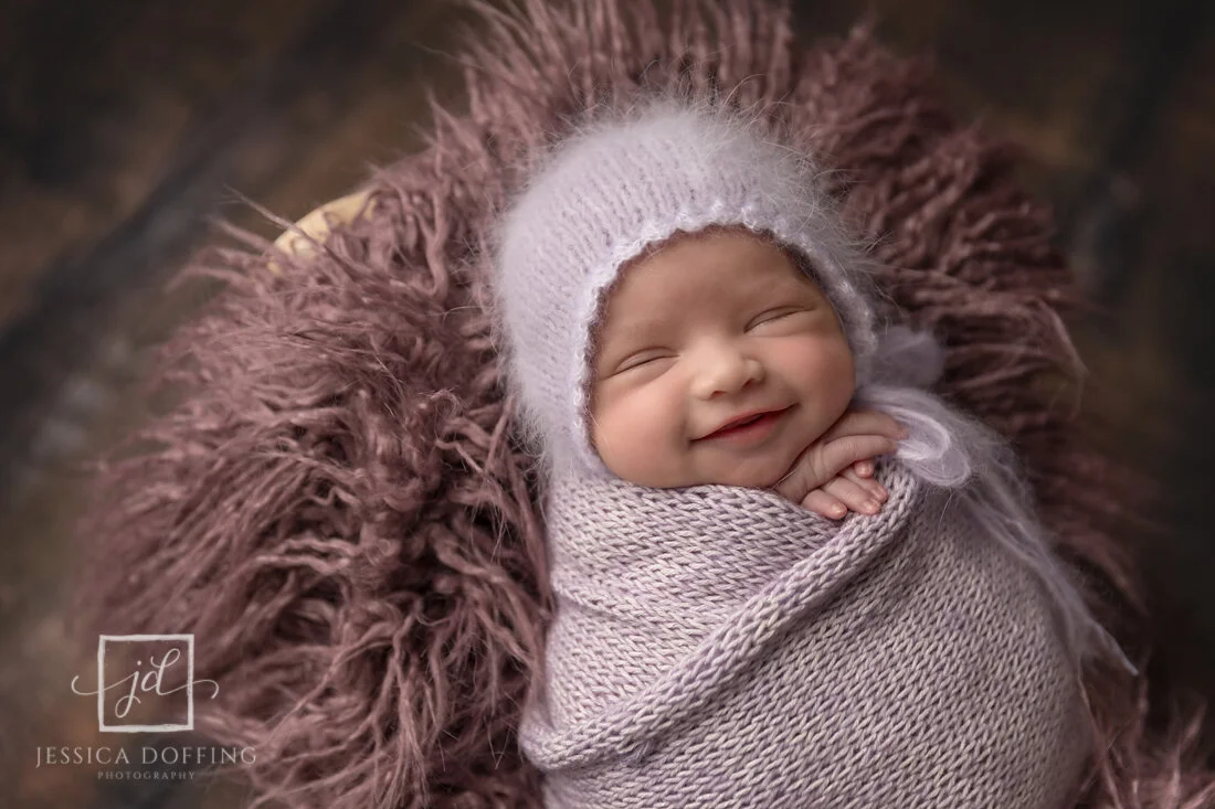 Smiling newborn baby girl wrapped in a soft lavender knit wrap during her Austin newborn photography session.