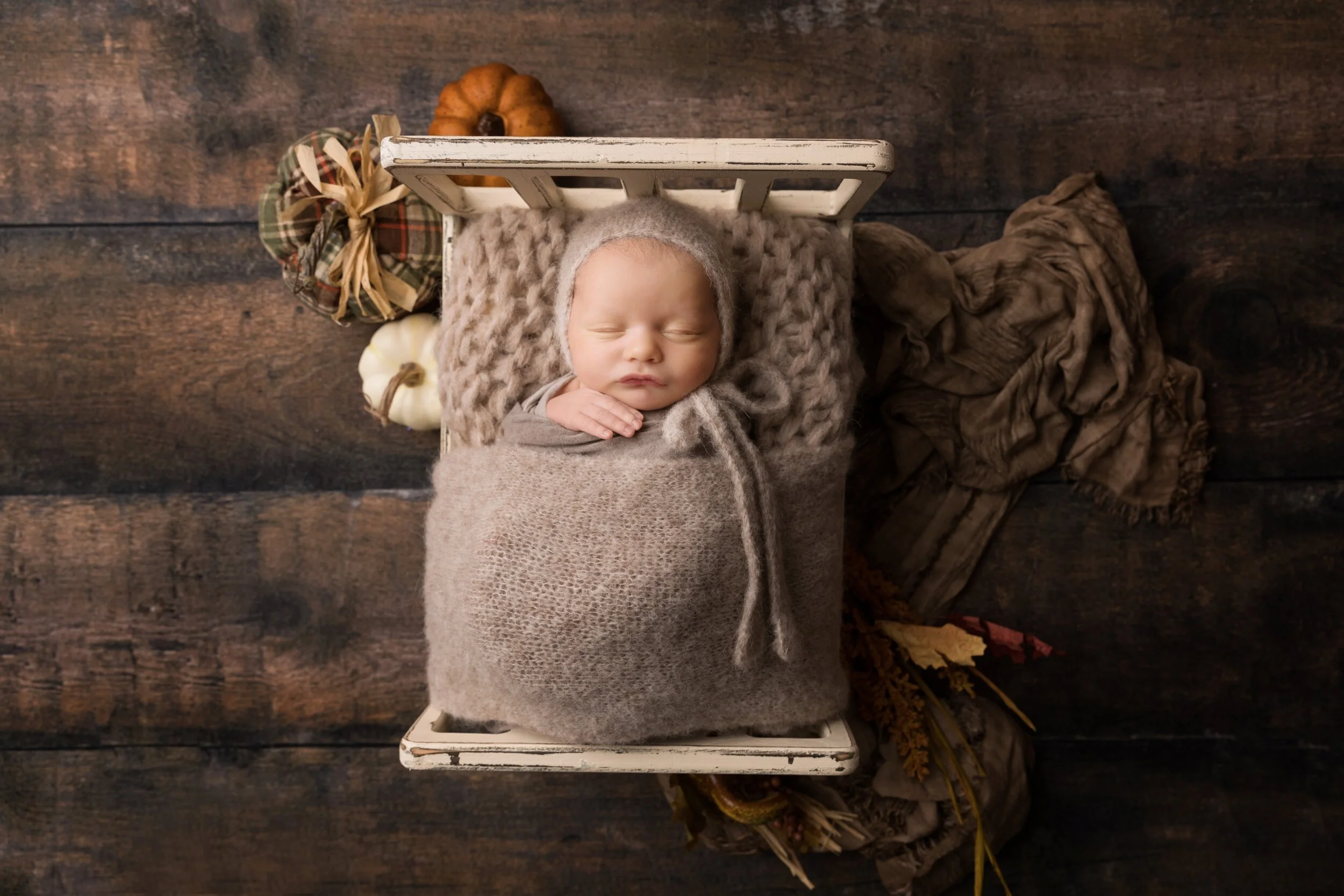Baby Nate sleeping peacefully in a wooden bed with cozy fall-themed styling during his Austin newborn photography session.