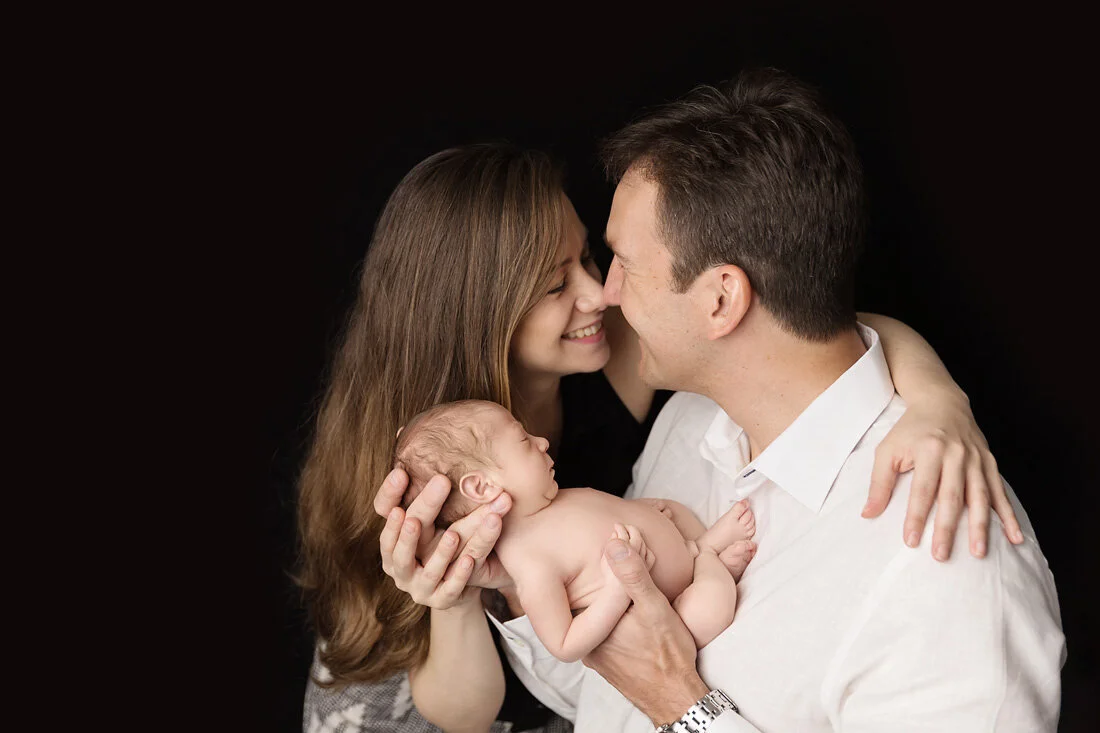 Parents smiling at each other while holding their newborn during a family newborn photography session in Austin, Texas.