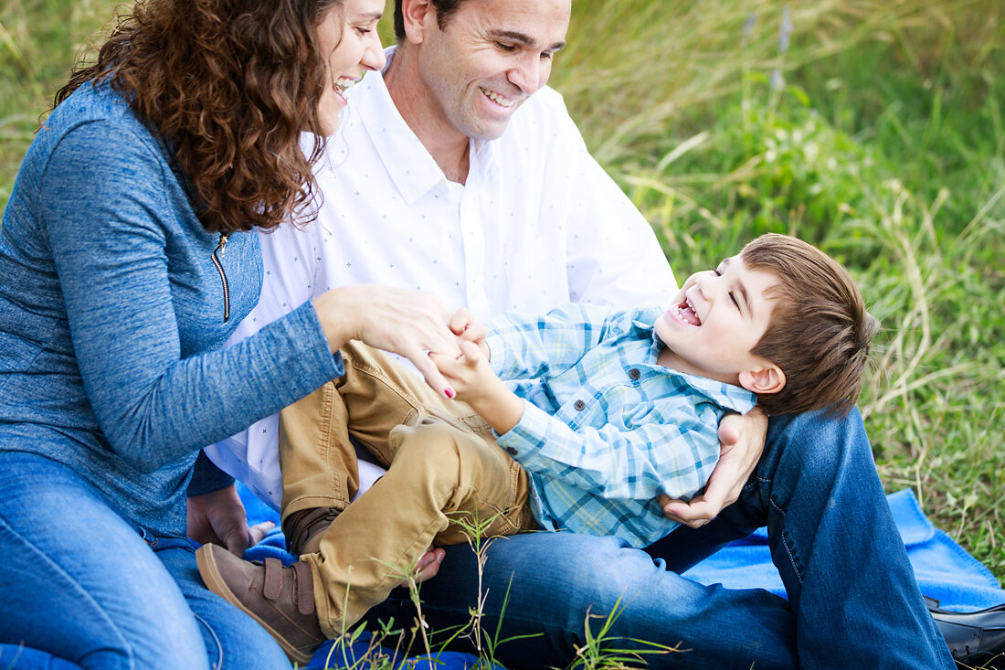 Parents playing and tickling their laughing toddler during a relaxed outdoor family photo session in Austin
