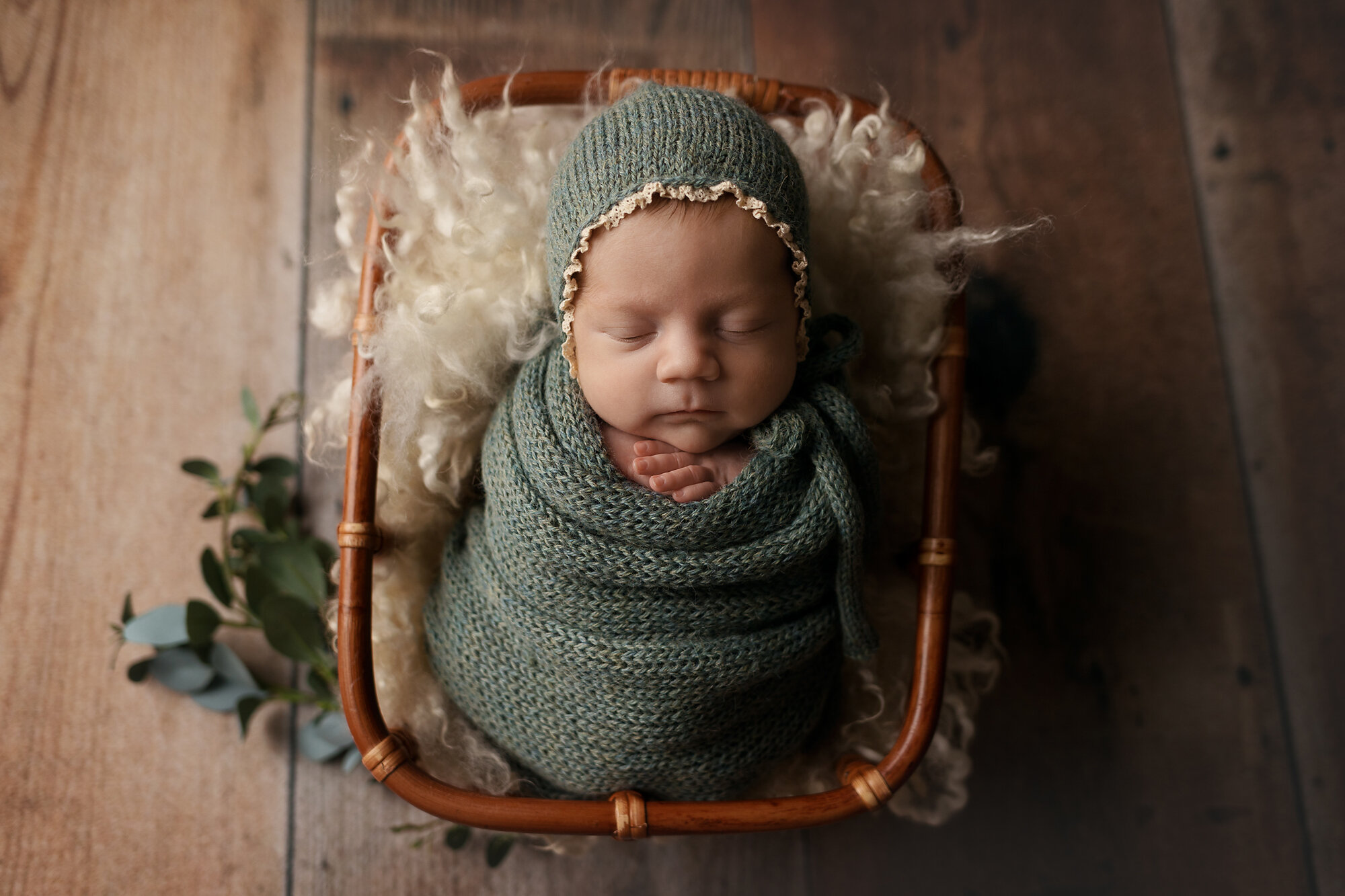 newborn girl in basket with green wrap and bonnet