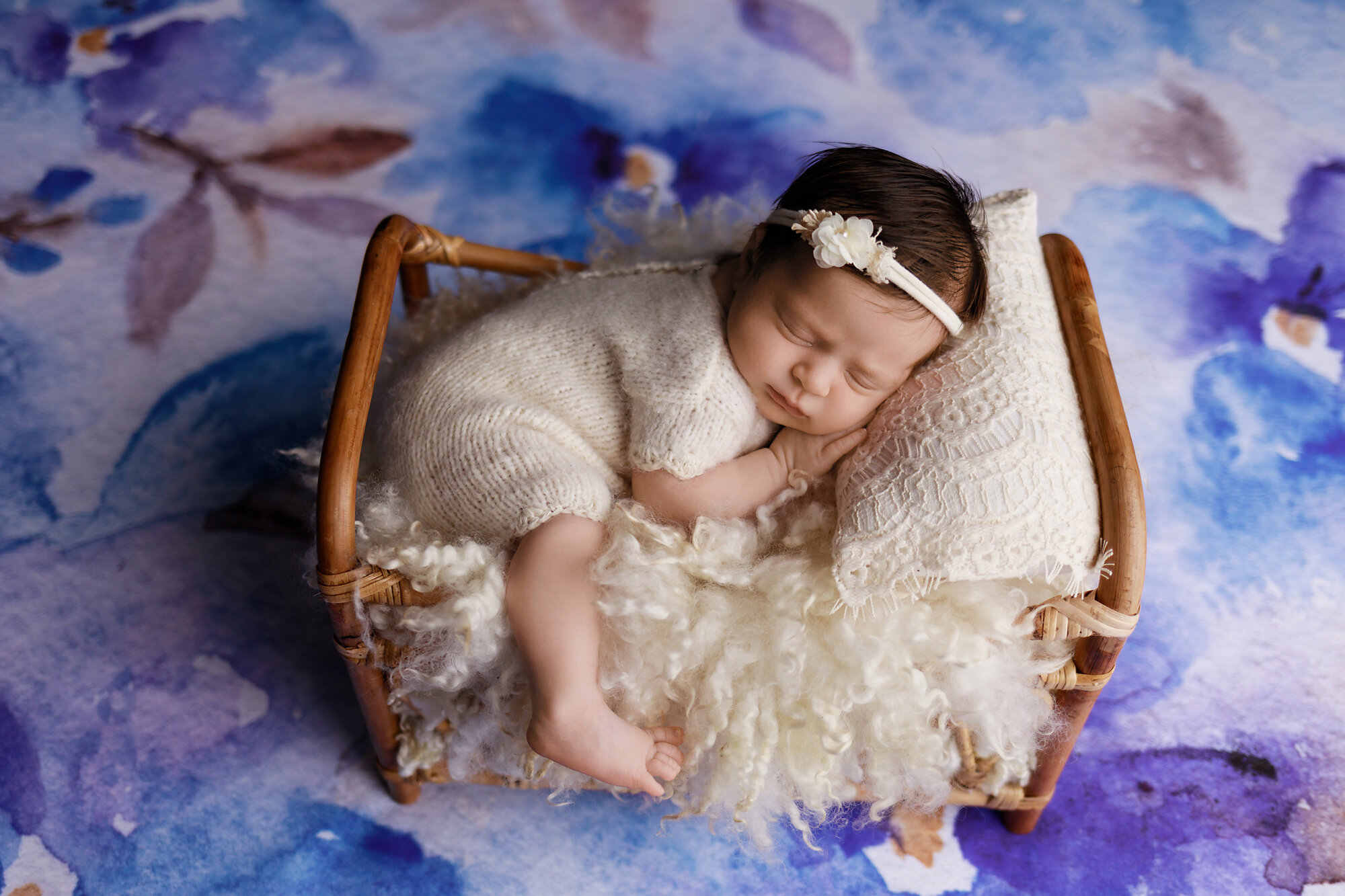 newborn girl sleeping on fluffy bed with blue floral background