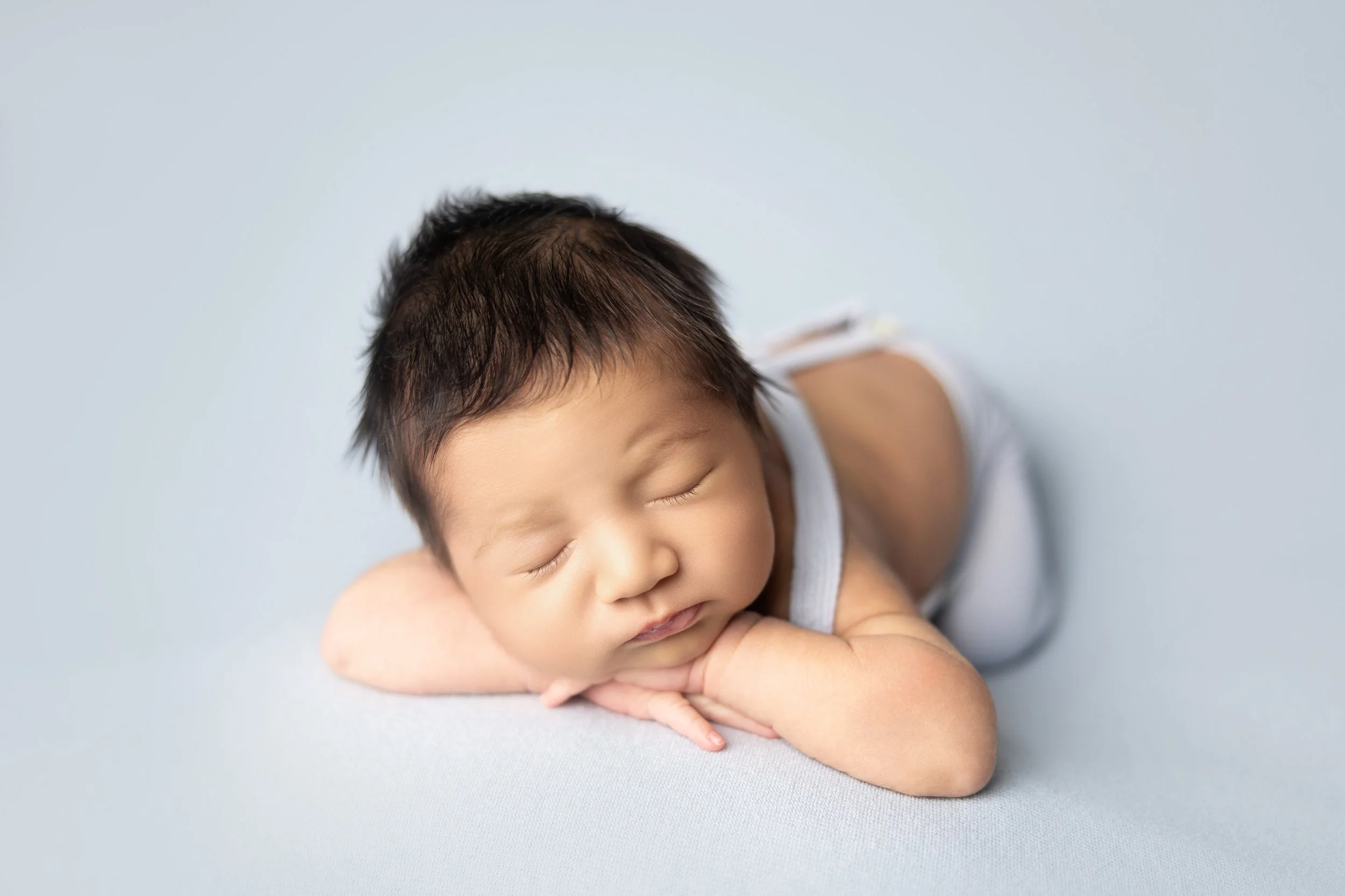 newborn-chin-on-hands-pose-blue-backdrop.jpg