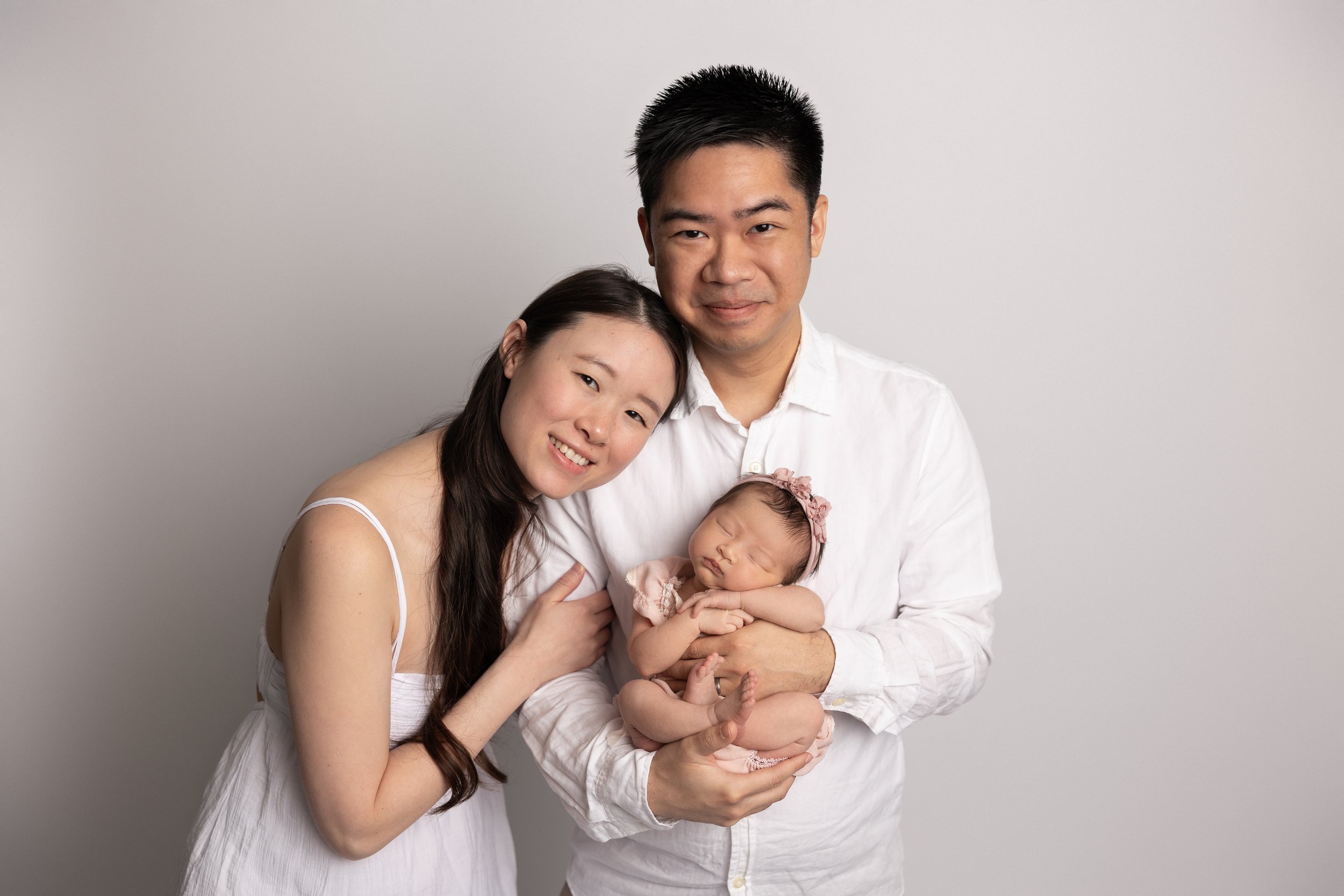 Parents holding their sleeping newborn daughter during a simple, timeless family portrait at a studio newborn photography session in Austin, Texas.