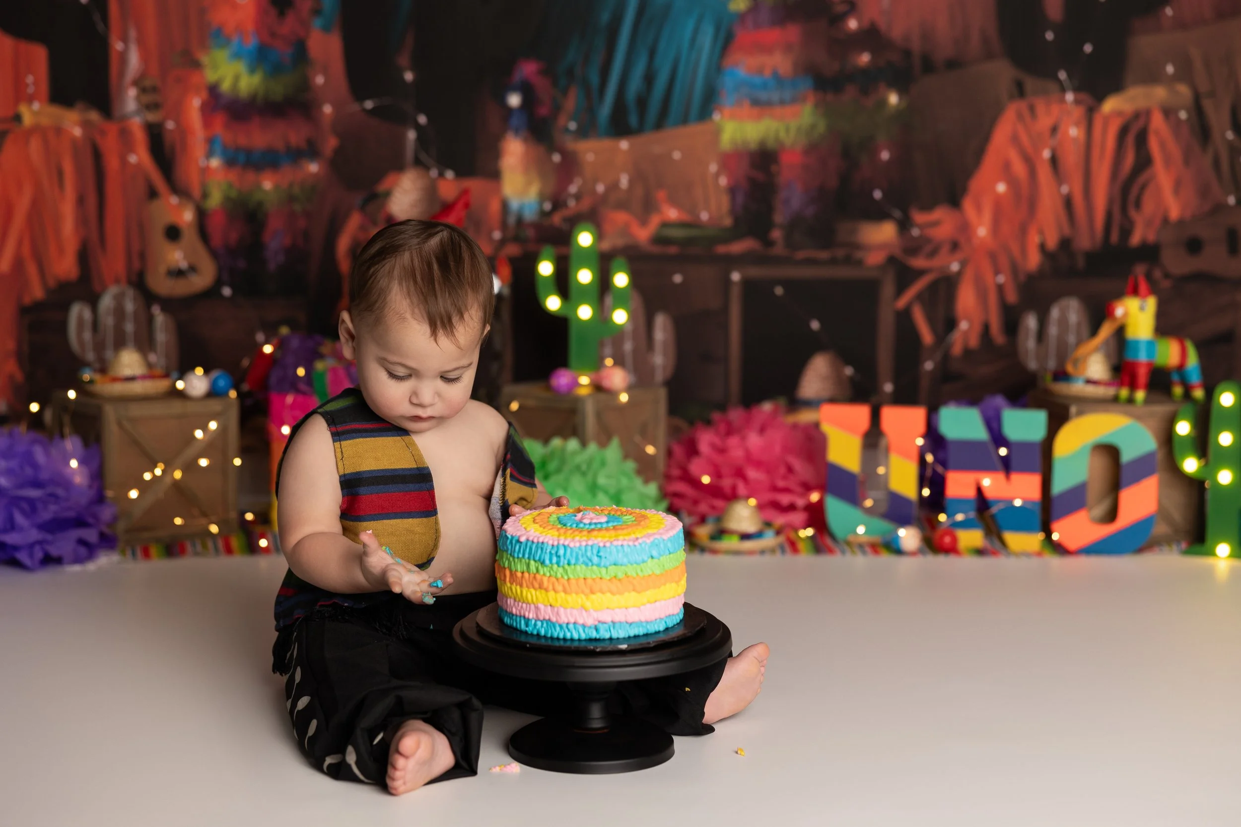 Fiesta cake smash – first birthday boy with rainbow cake and vibrant decor
