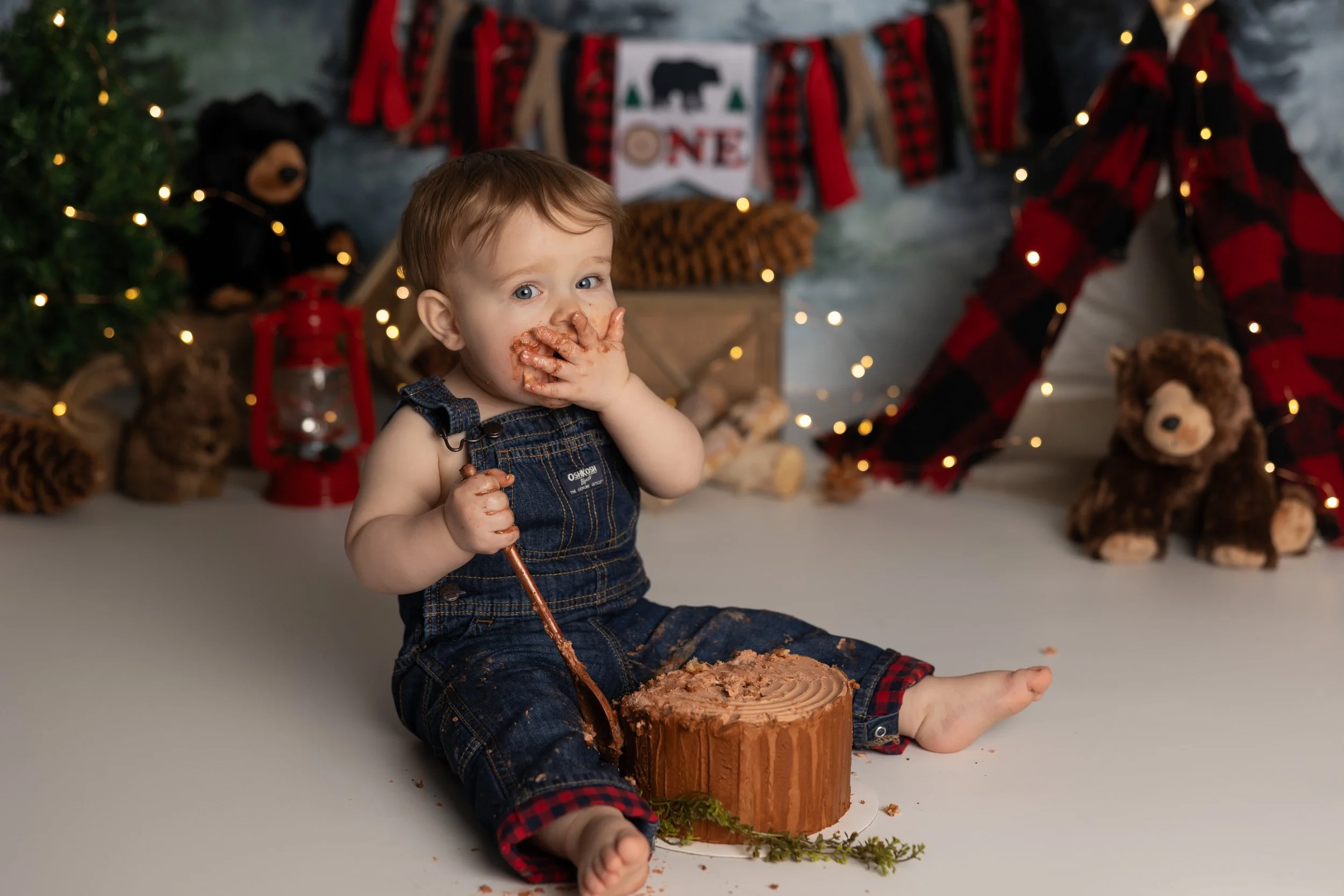One Happy Camper cake smash – first birthday boy enjoying cake with cozy camp theme