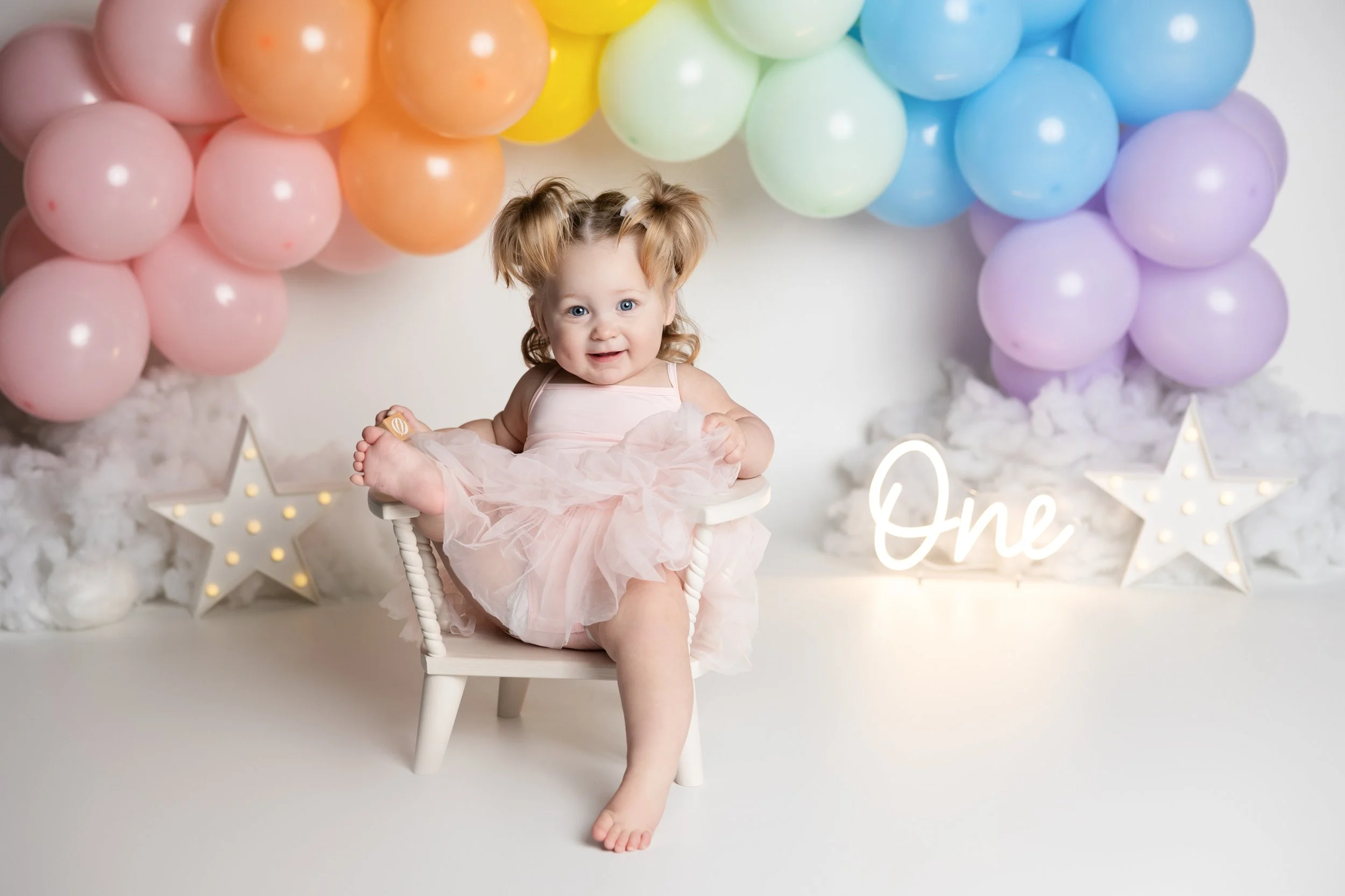 Simple rainbow cake smash theme – first birthday girl portrait with pastel balloons