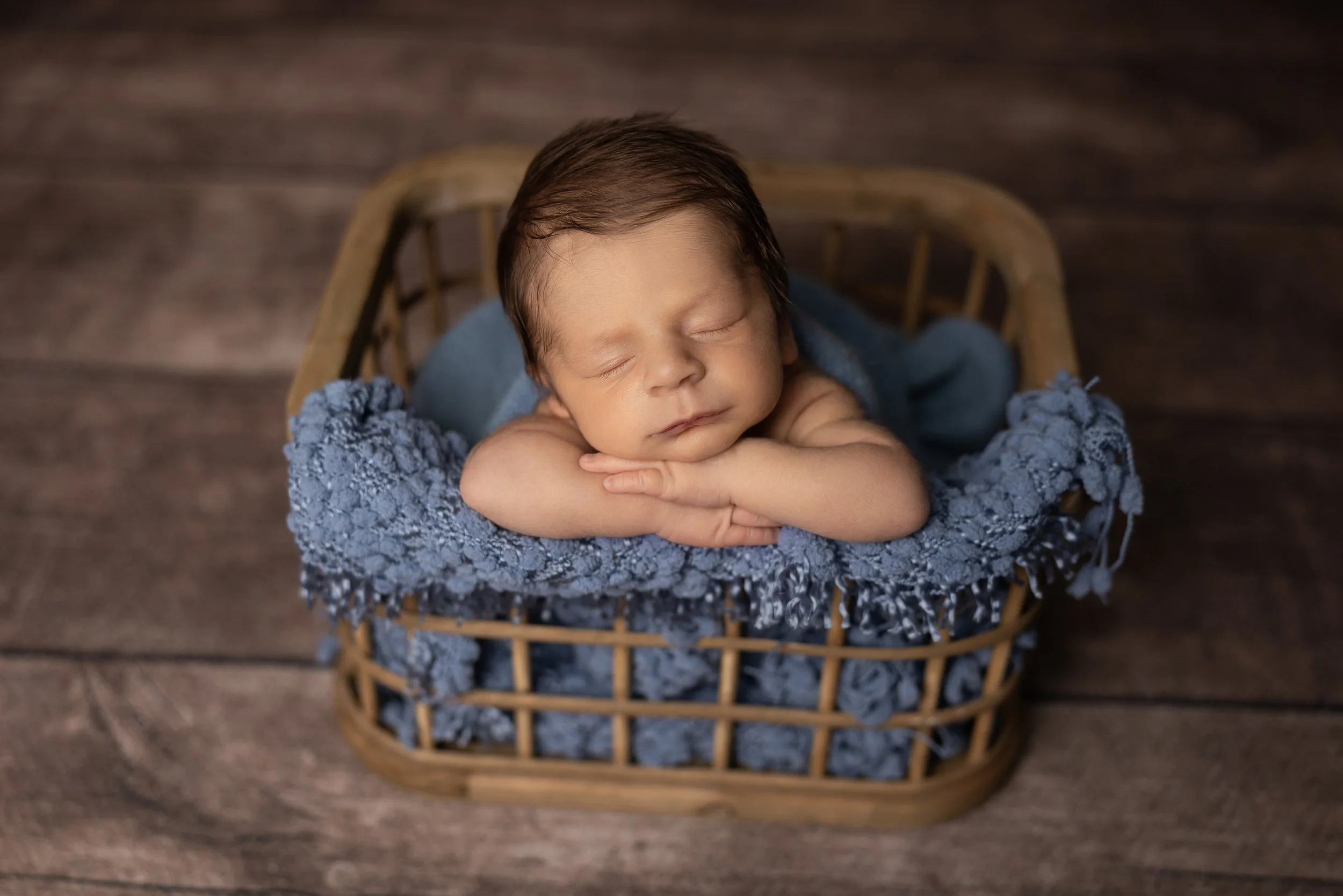 close-up of newborn baby boy in basket with chin resting on hands and peaceful expression