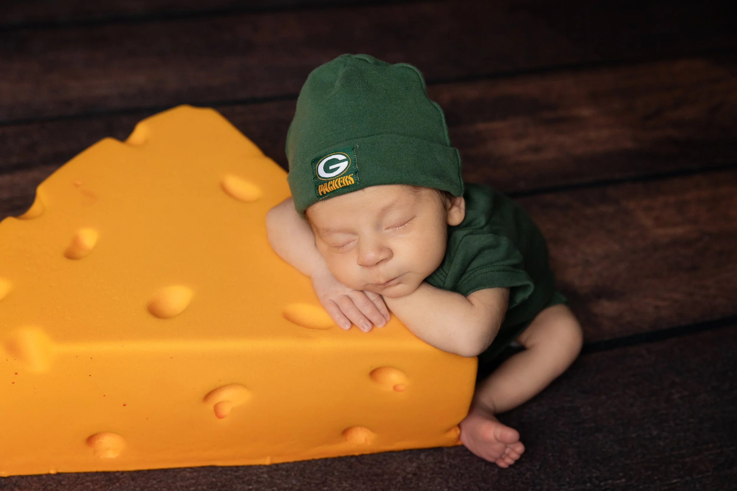 sleeping newborn baby boy resting on oversized cheese prop wearing green hat