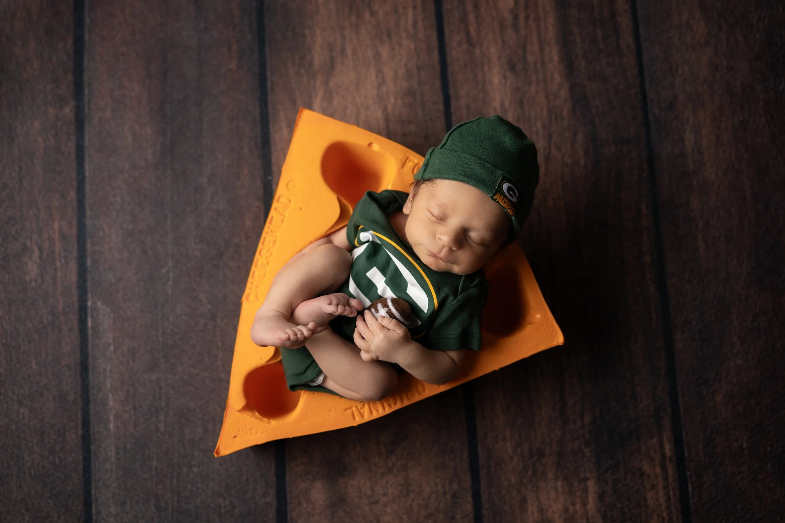 overhead view of newborn baby boy in green outfit lying on bright orange cheese prop