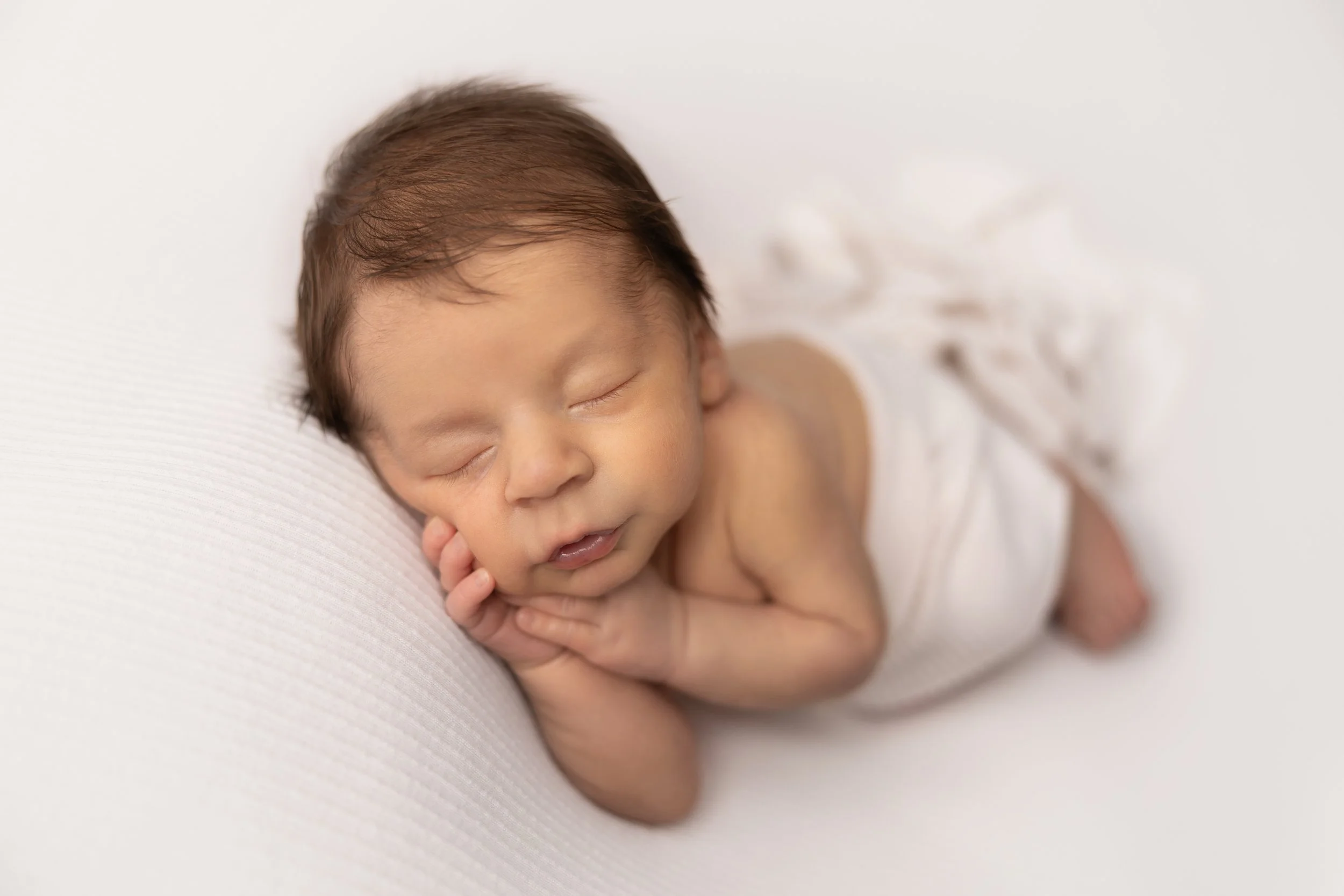 sleeping newborn baby boy resting cheek on hand on white textured backdrop