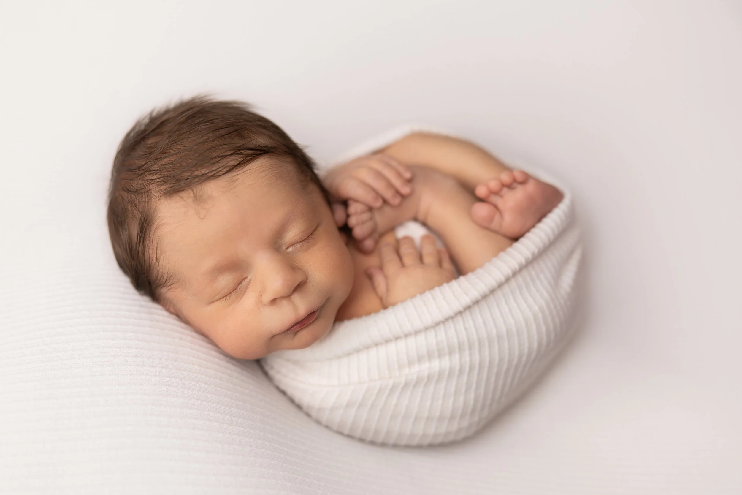 newborn baby wrapped in white fabric sleeping in small round prop