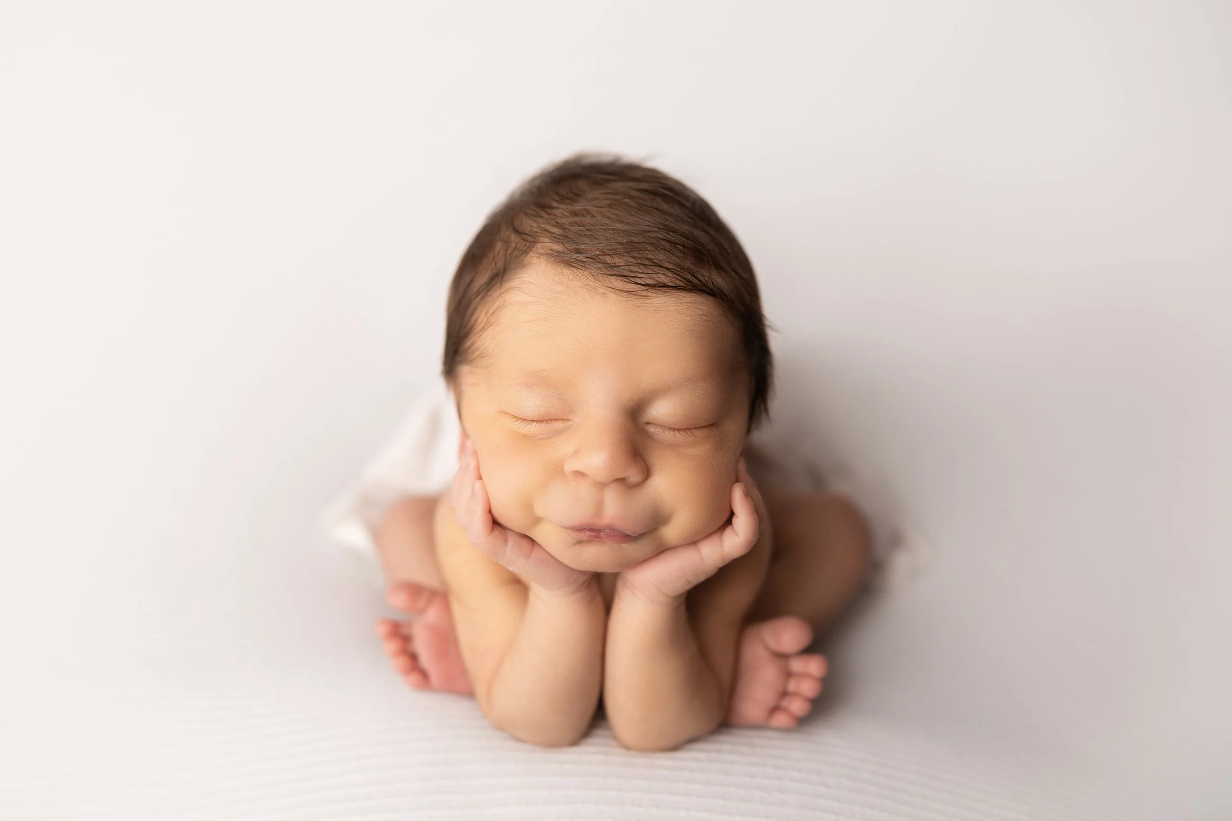 newborn baby boy posed with chin in hands on white backdrop (composite safety pose)