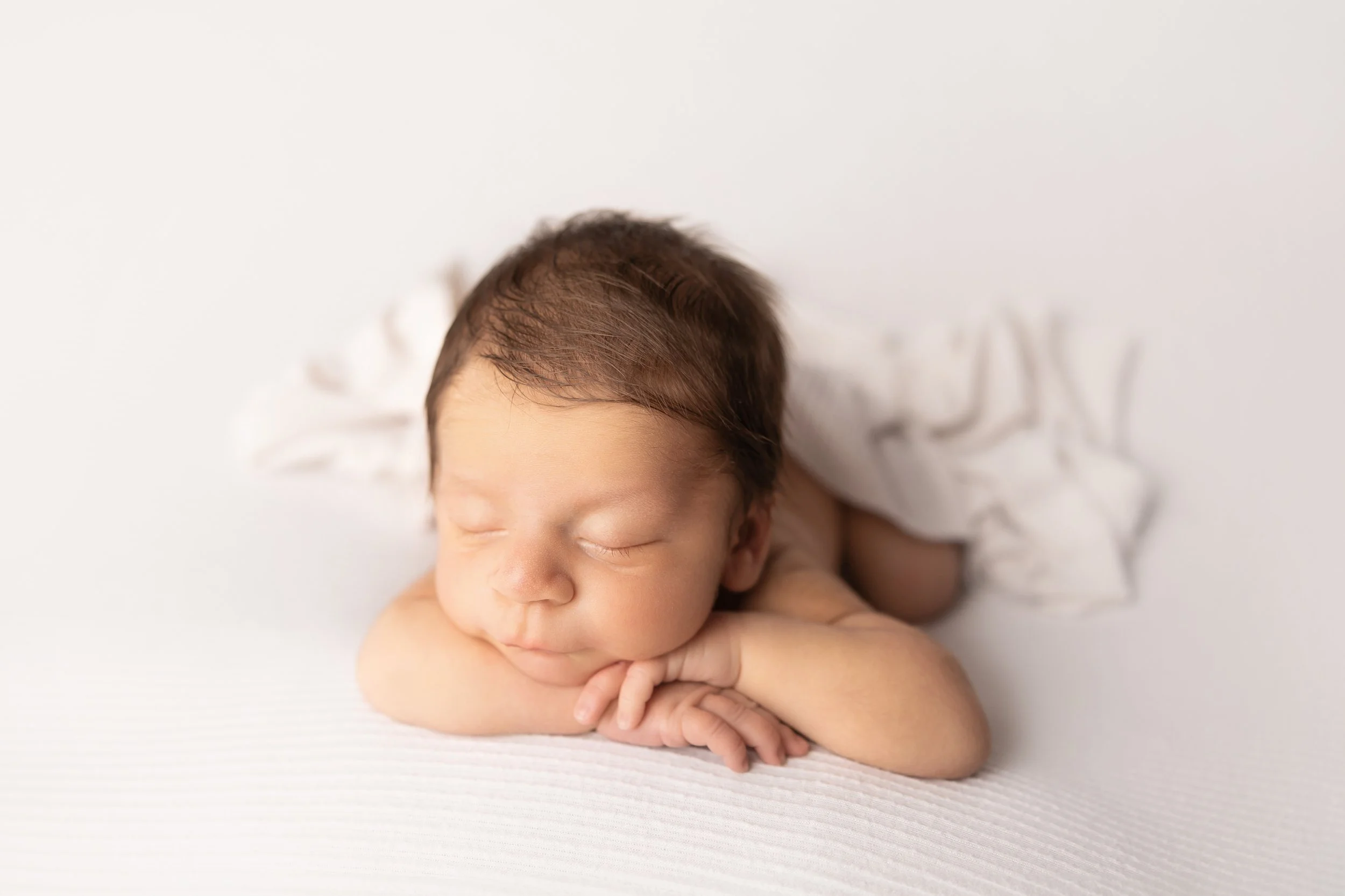sleeping newborn baby boy with chin resting on hands on soft white background