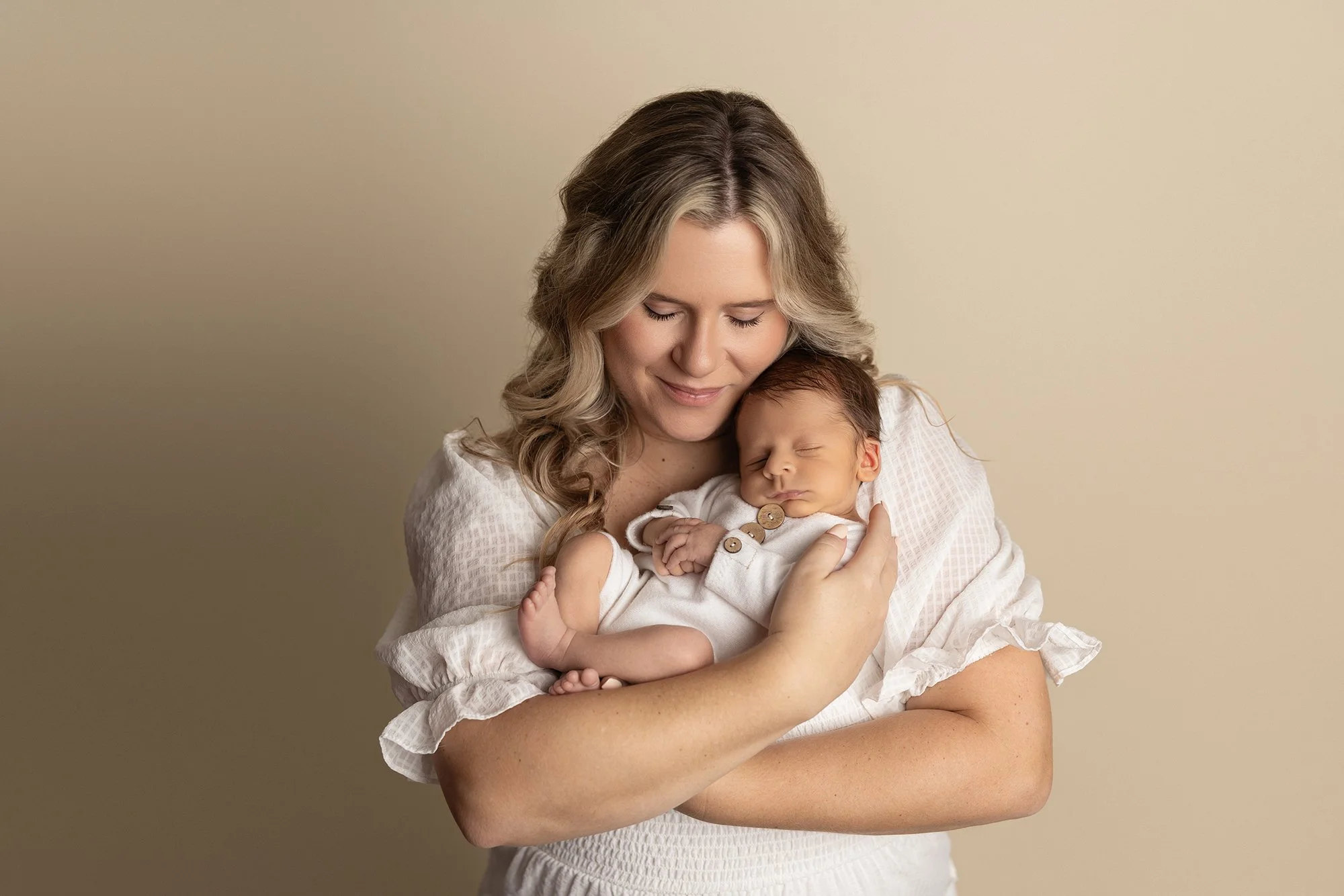 mother holding newborn baby close with soft smile against neutral background