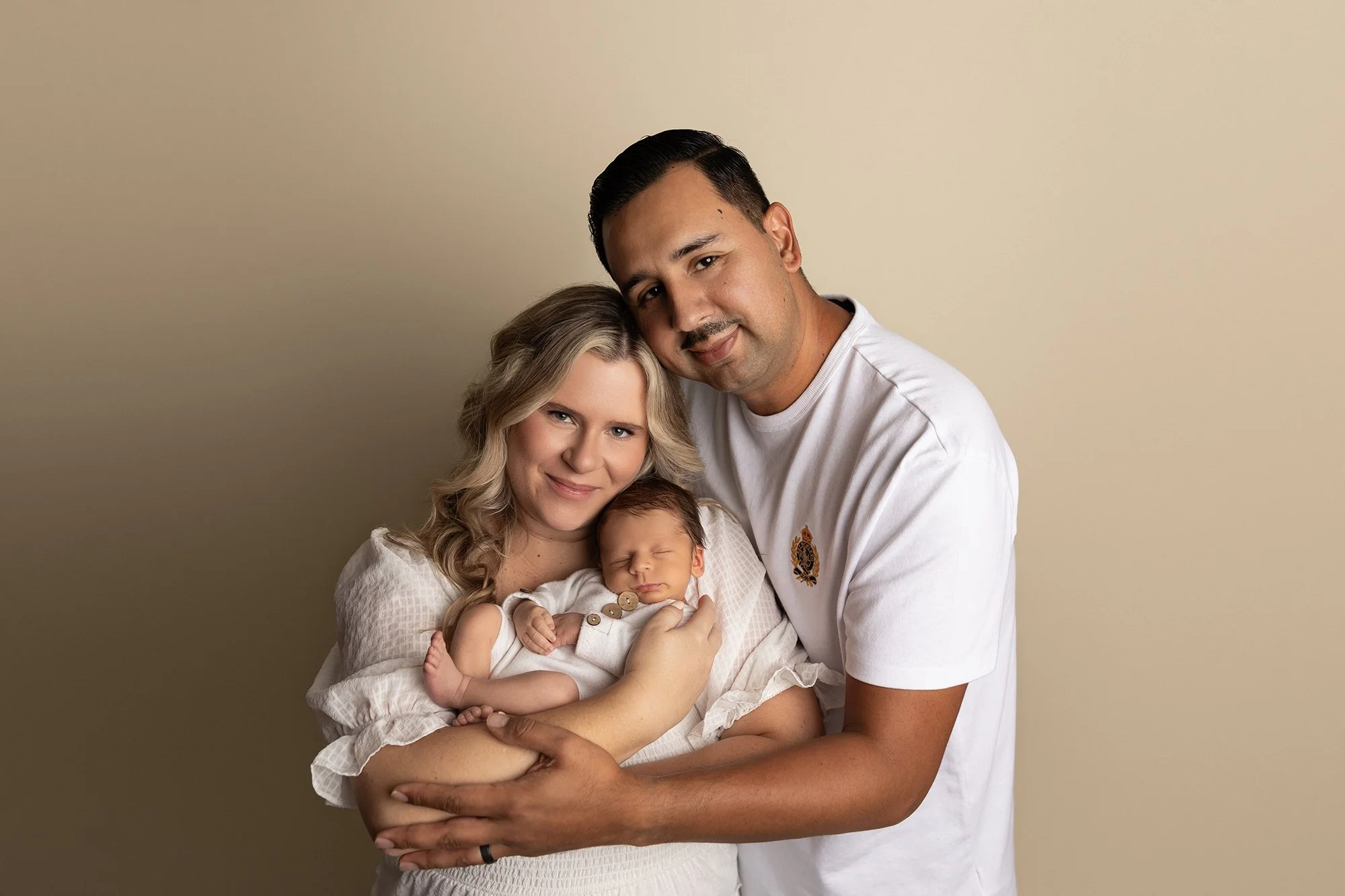 parents holding newborn baby together smiling at camera in studio