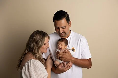 parents smiling down at newborn baby during relaxed family portrait