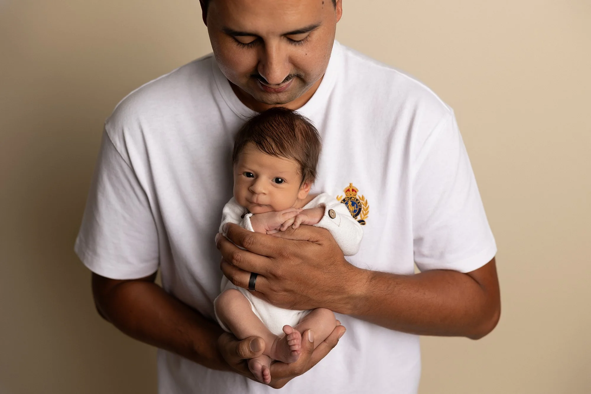 father holding newborn baby upright looking down in soft studio lighting