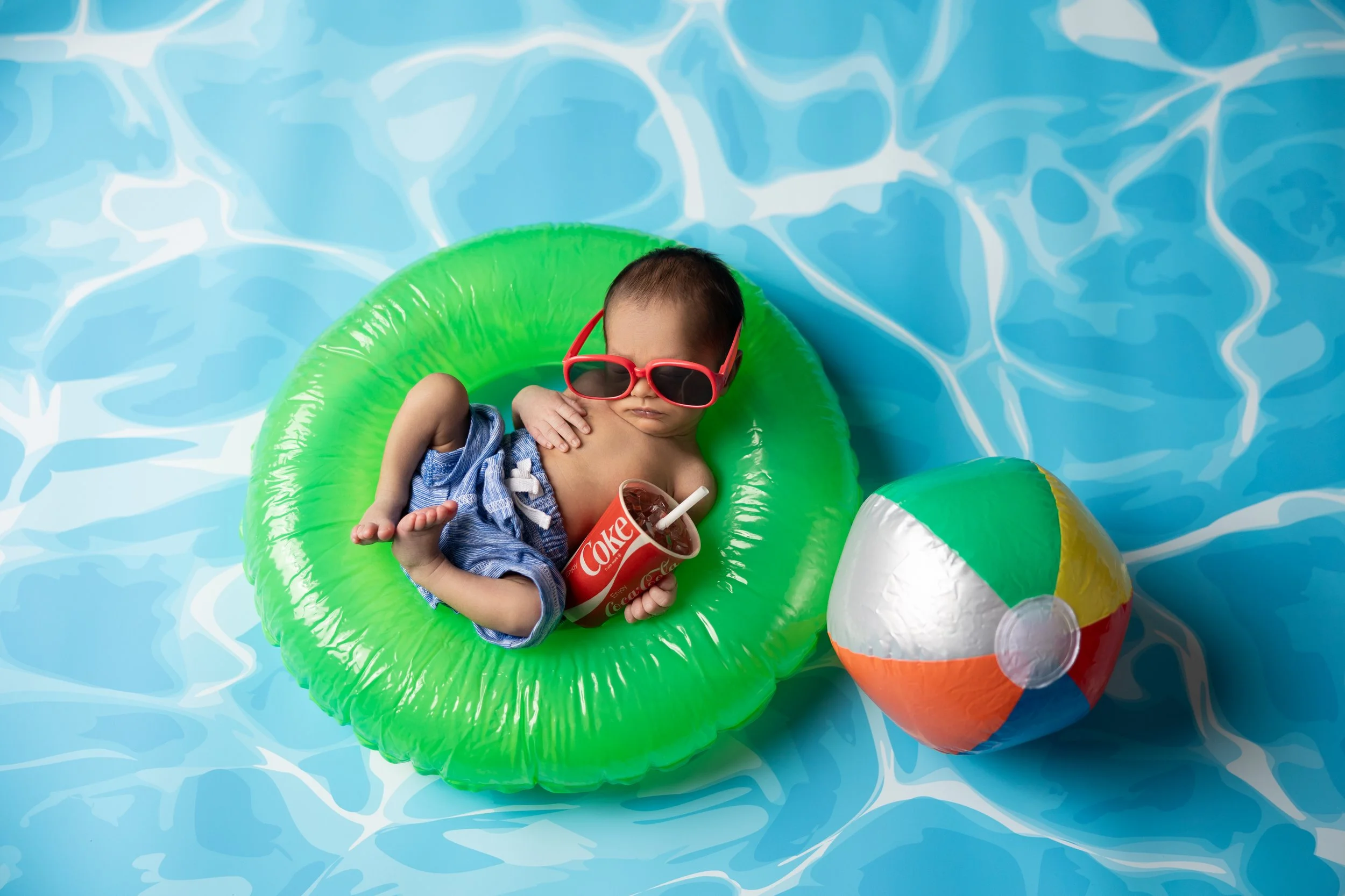 Newborn in green float with sunglasses and beach ball