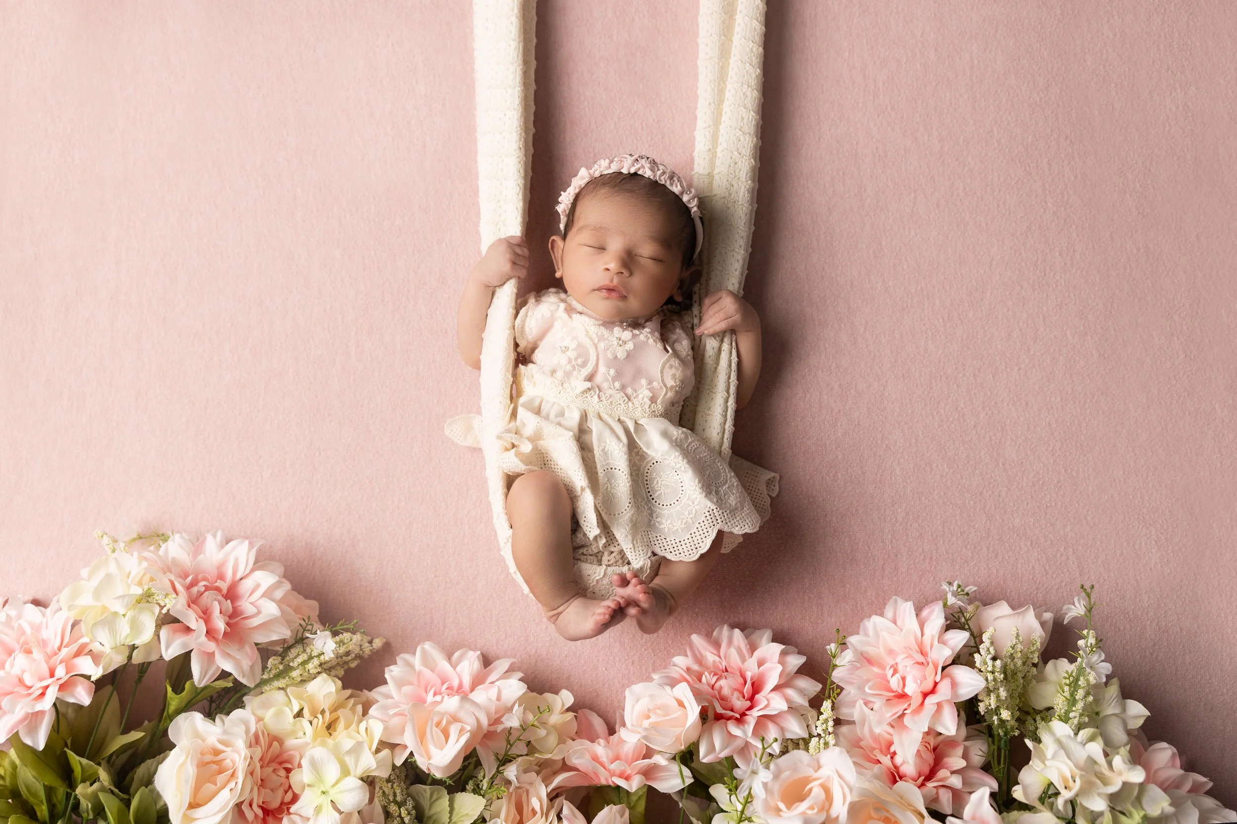 Newborn posed on swing with soft greenery backdrop