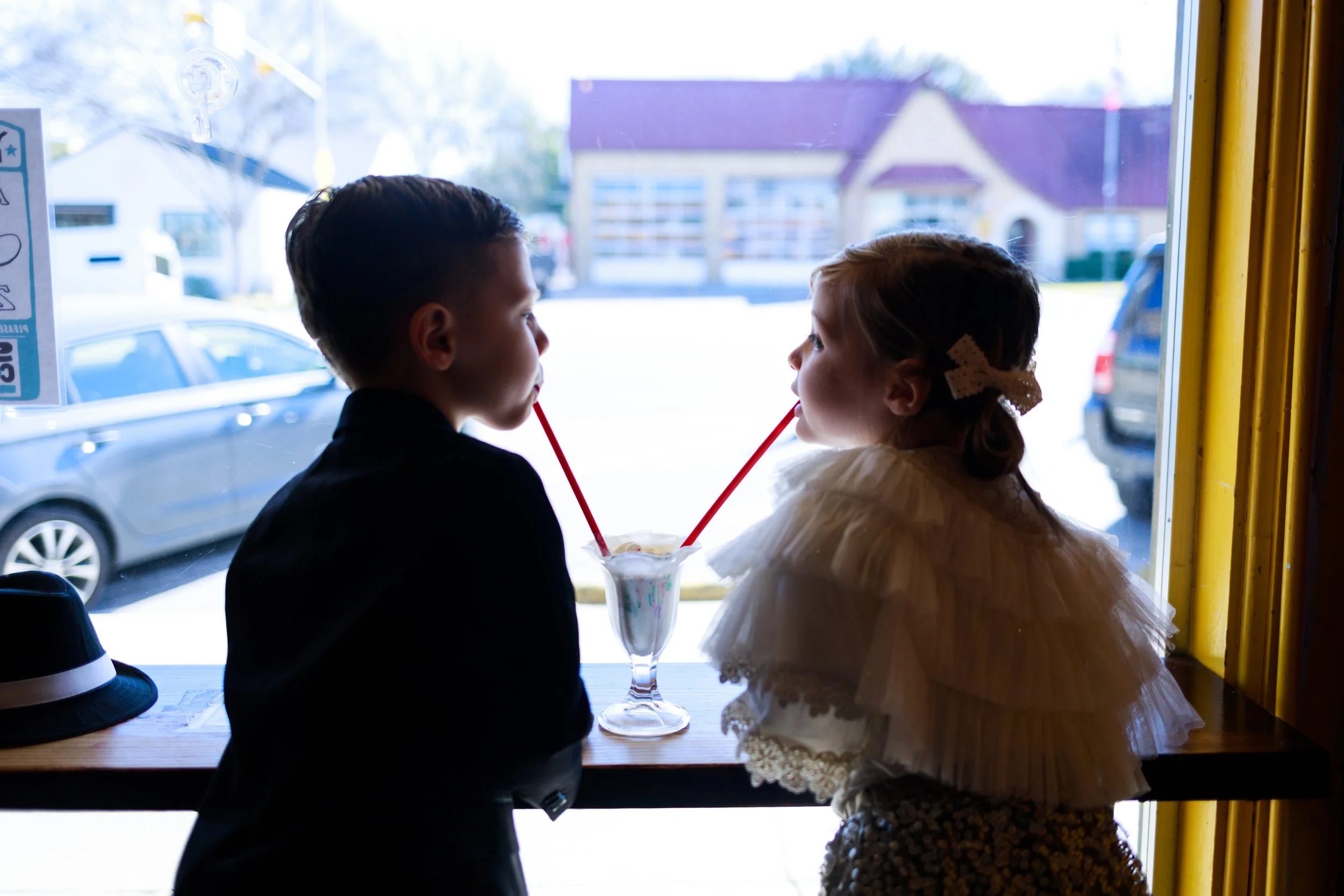 Twins sharing milkshake at window in Austin