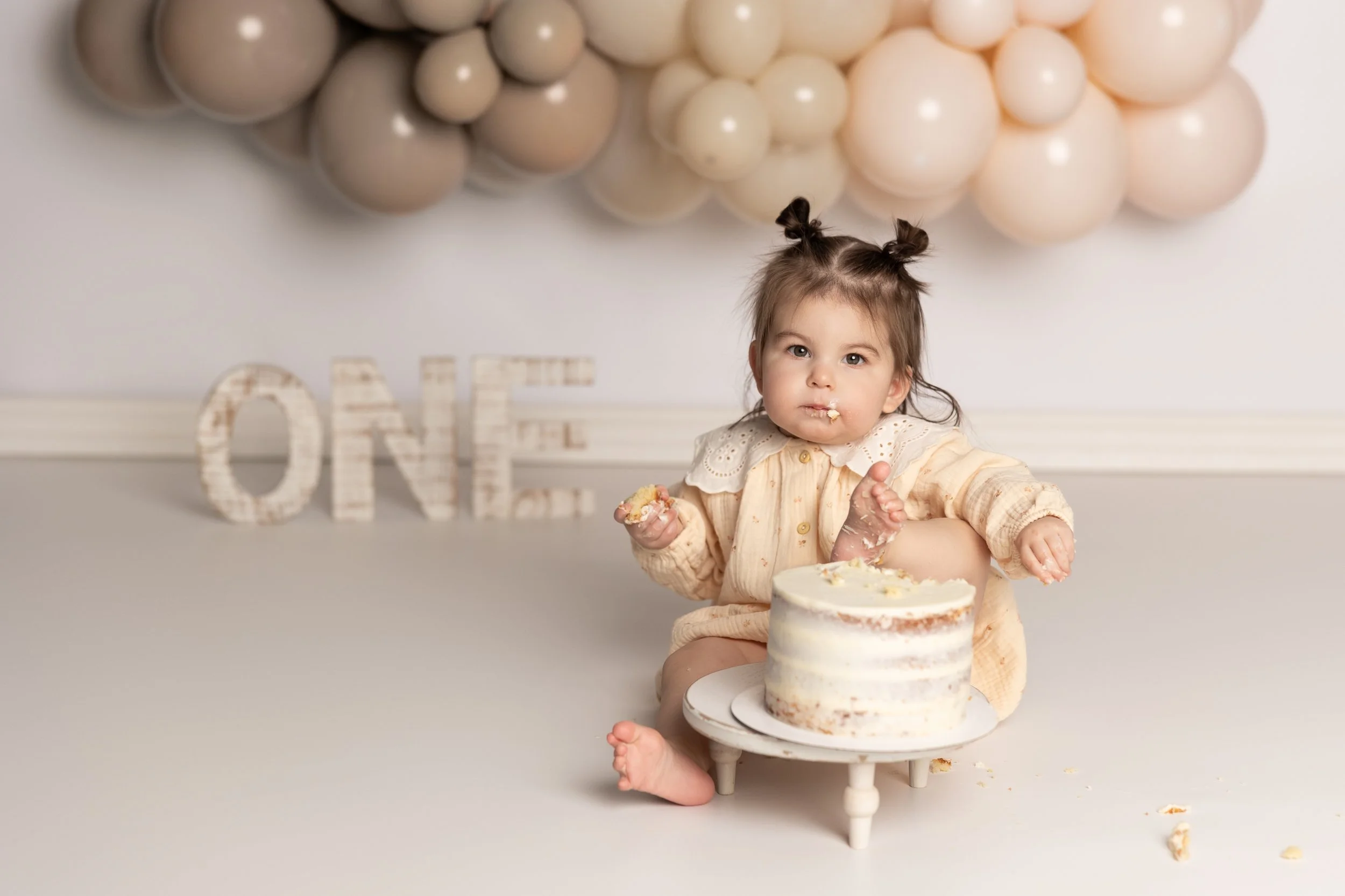 Simple neutral-toned cake smash session featuring soft balloons and a minimalist birthday setup.