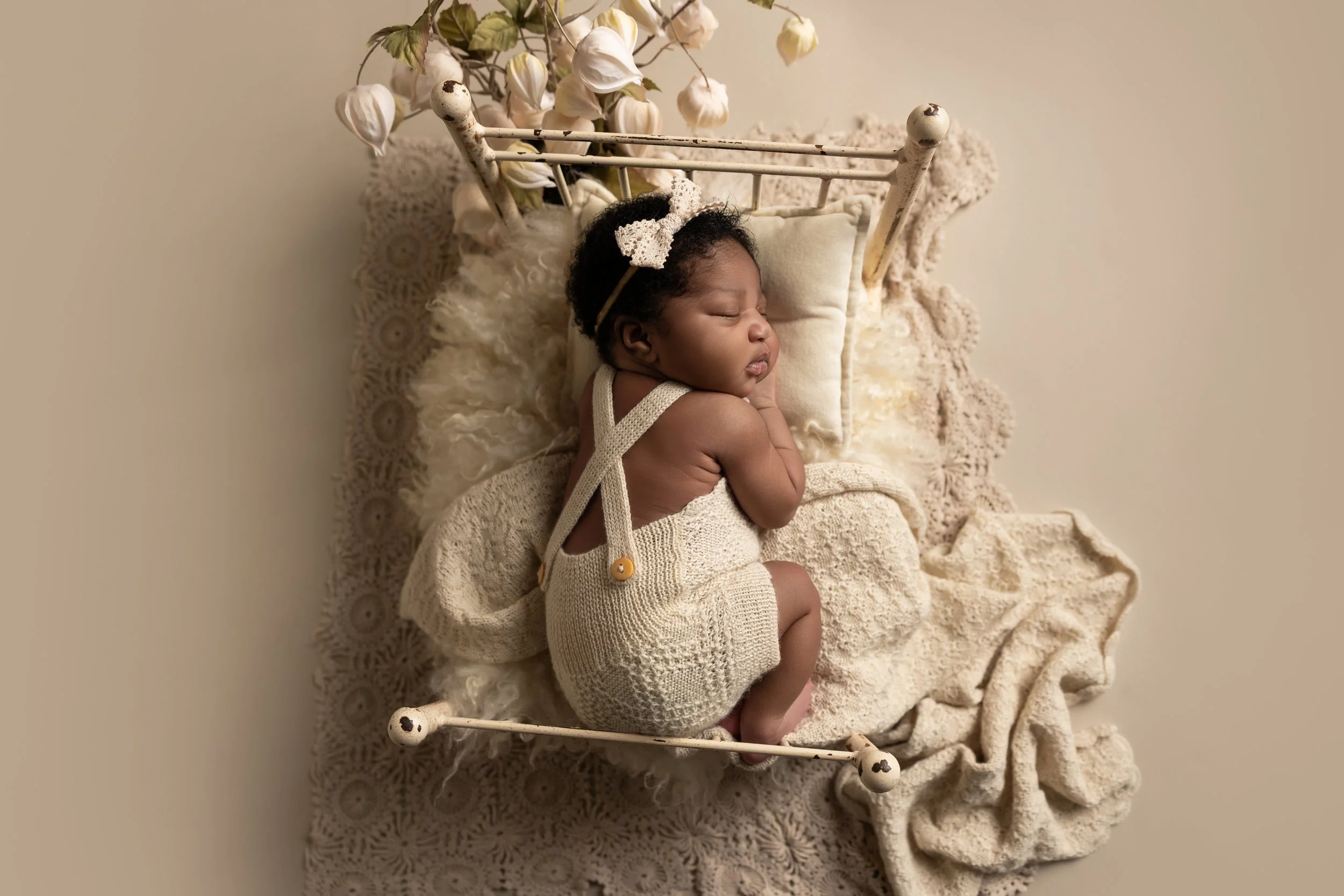 Newborn posed in a vintage bed prop, one of the essential newborn photography props recommended for beginner posed newborn photographers.