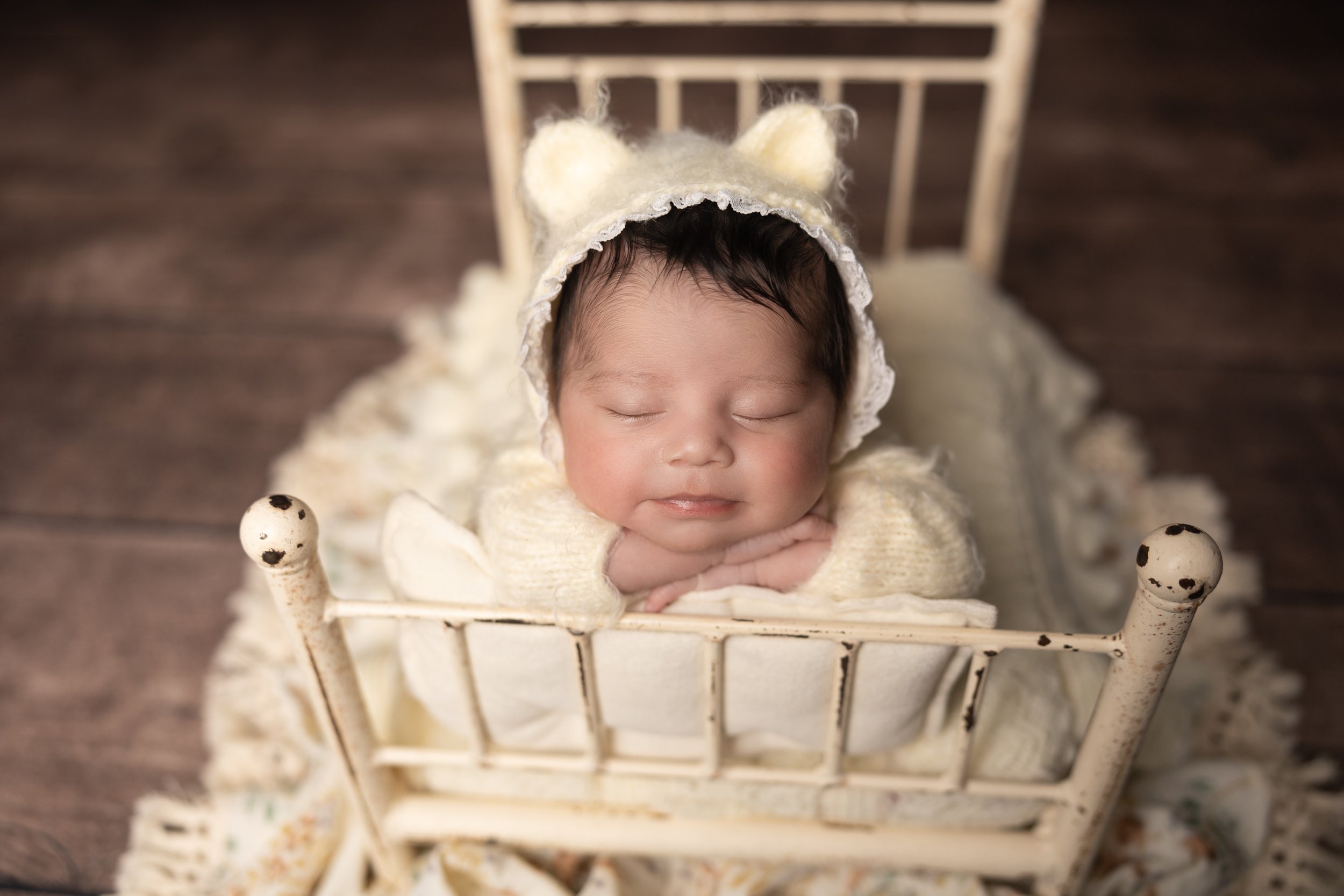 Sleeping newborn posed with chin resting on hands in a vintage bed prop, demonstrating a classic newborn photography pose.