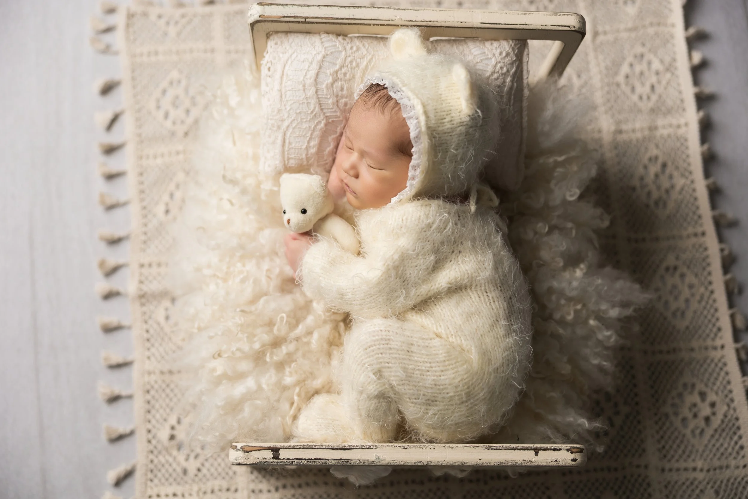newborn baby girl in cream outfit with matching monochromatic background holding bear
