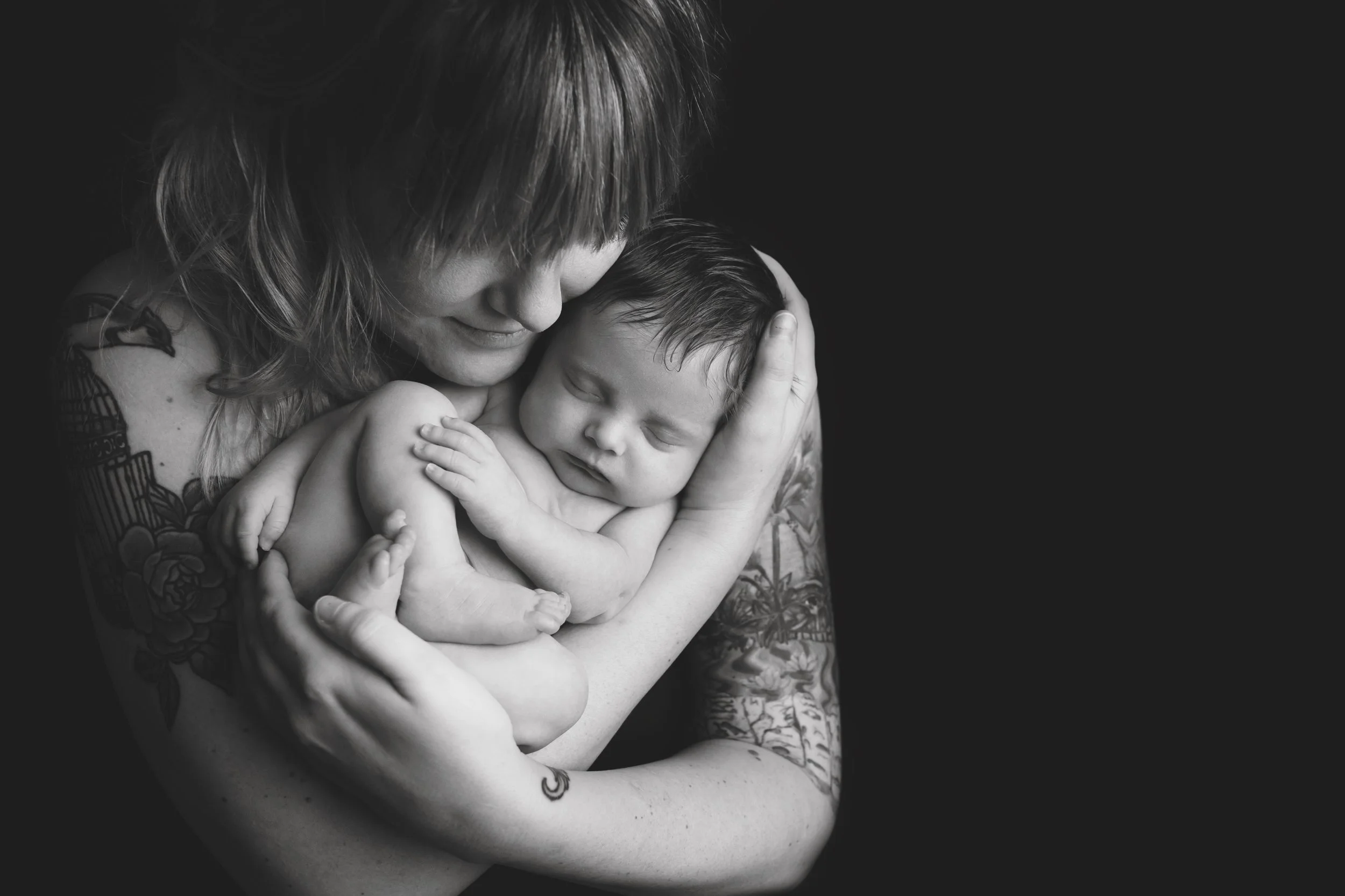 Black and white portrait of a mother holding her newborn close in an intimate studio photography session.