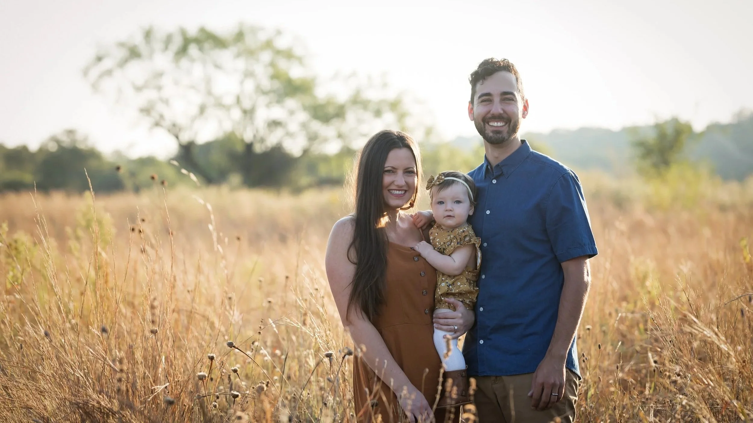Family of three standing together in golden fall grass during an outdoor portrait session at Commons Ford Ranch in Austin, Texas.