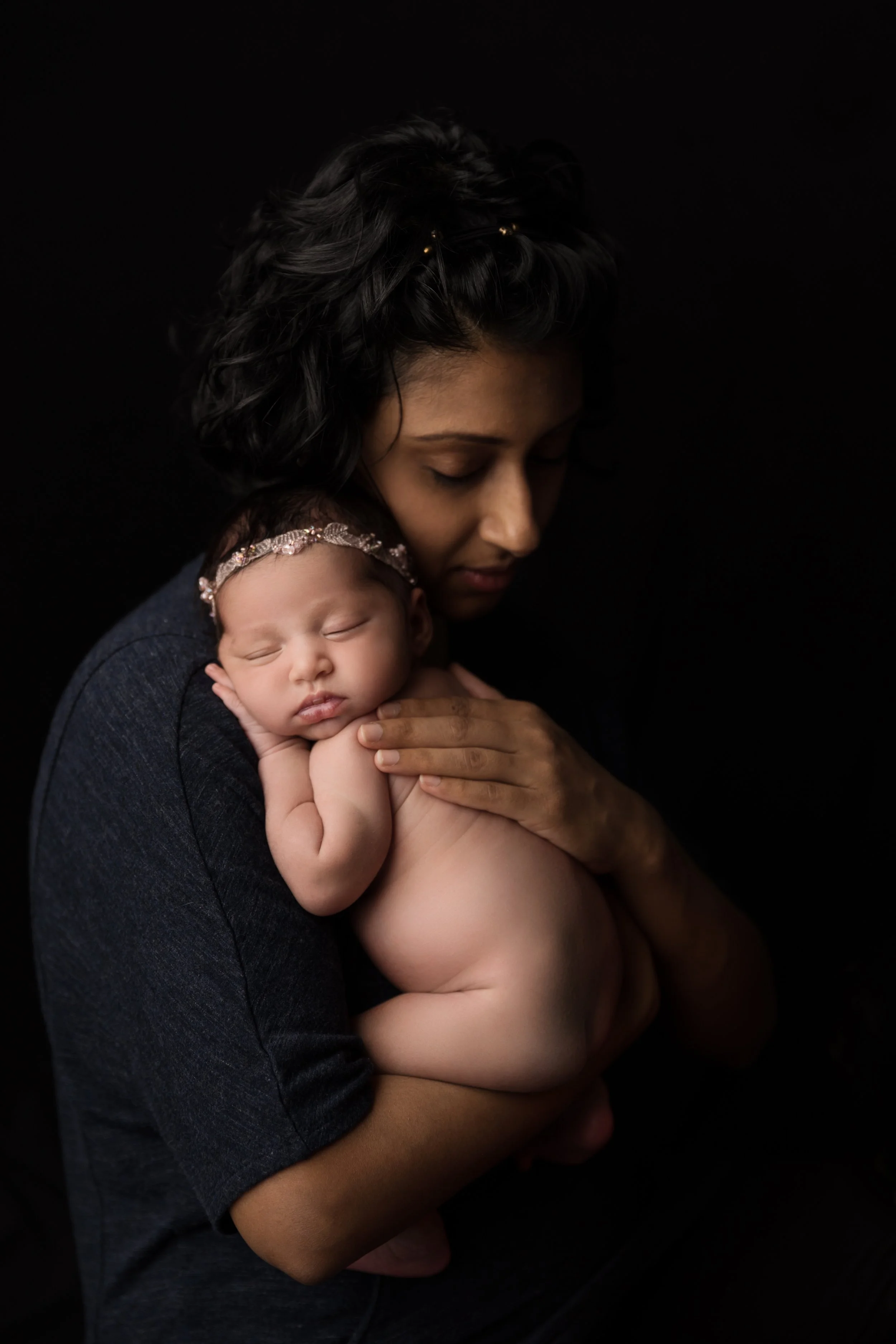 Mother cuddling sleeping newborn during a dark and moody studio portrait session