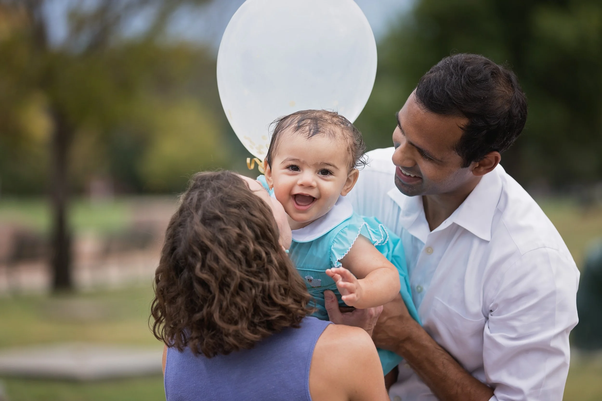 Parents holding and smiling at their one year old baby during an outdoor first birthday photo session at Butler Park in Austin Texas