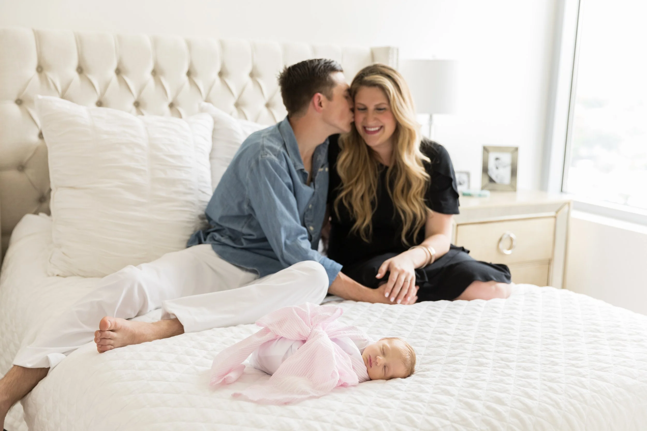 newborn baby girl lying on bed with parents in the background