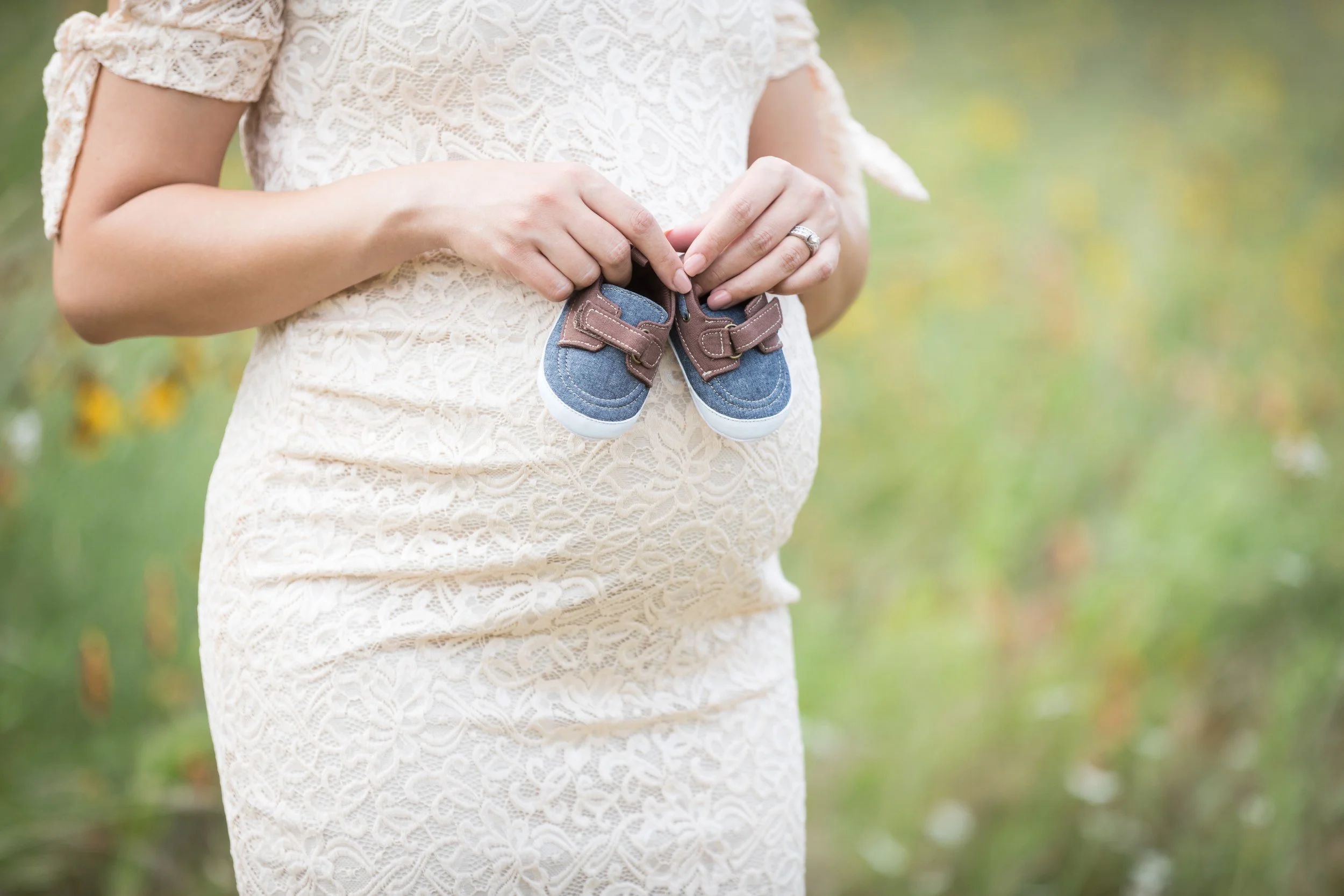 Expectant mother holding baby shoes during pregnancy, illustrating the ideal time to book newborn photos in Austin, Texas.