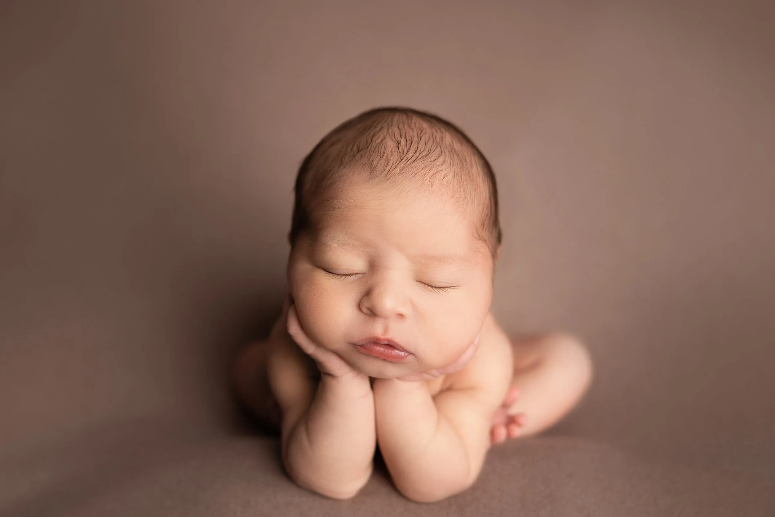 newborn baby boy posed in froggy position on brown backdrop in Austin Tx studio