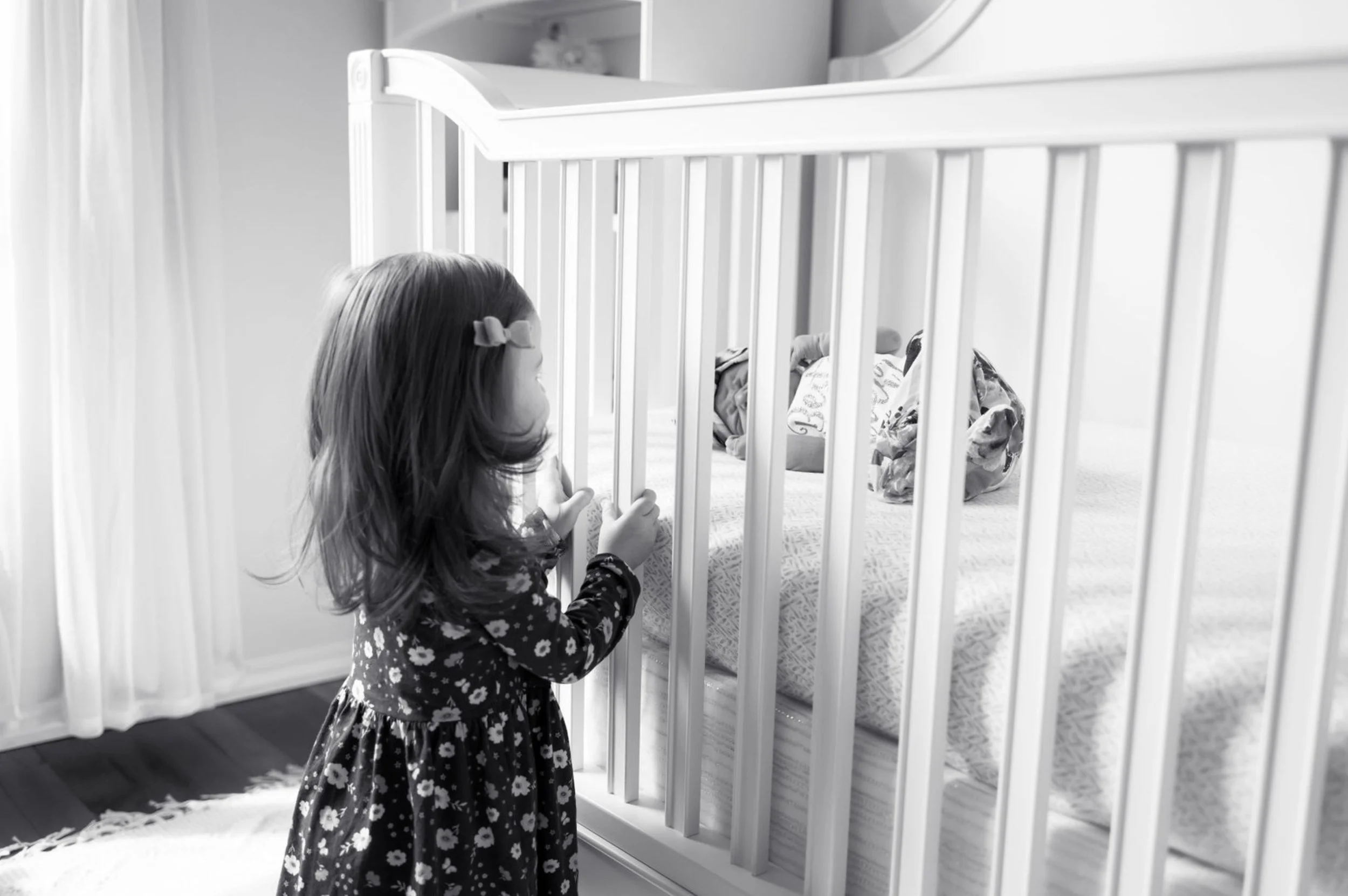 Toddler looking into a crib at a newborn baby during an Austin lifestyle newborn photography session.