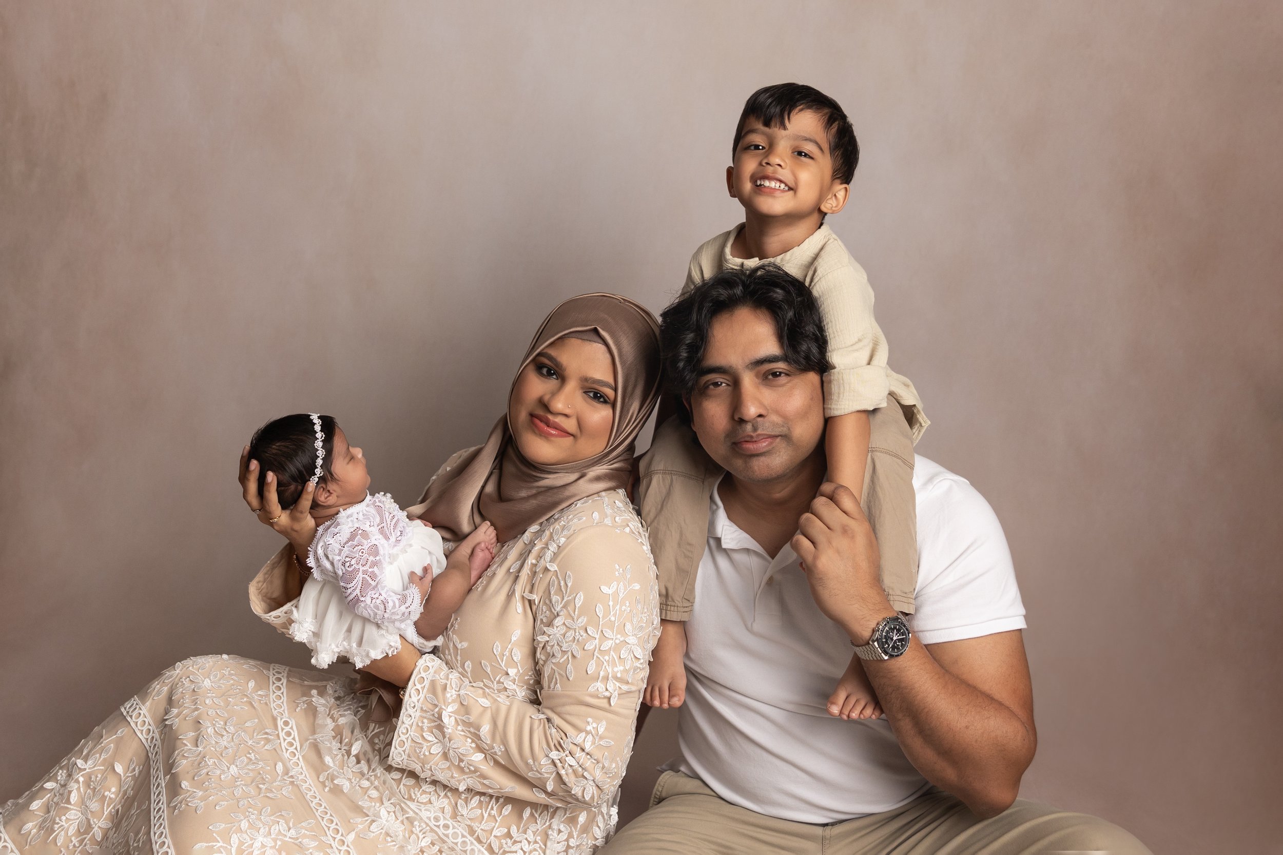 Parents and older sibling posing together with their newborn baby during a family newborn photography session in an Austin studio.