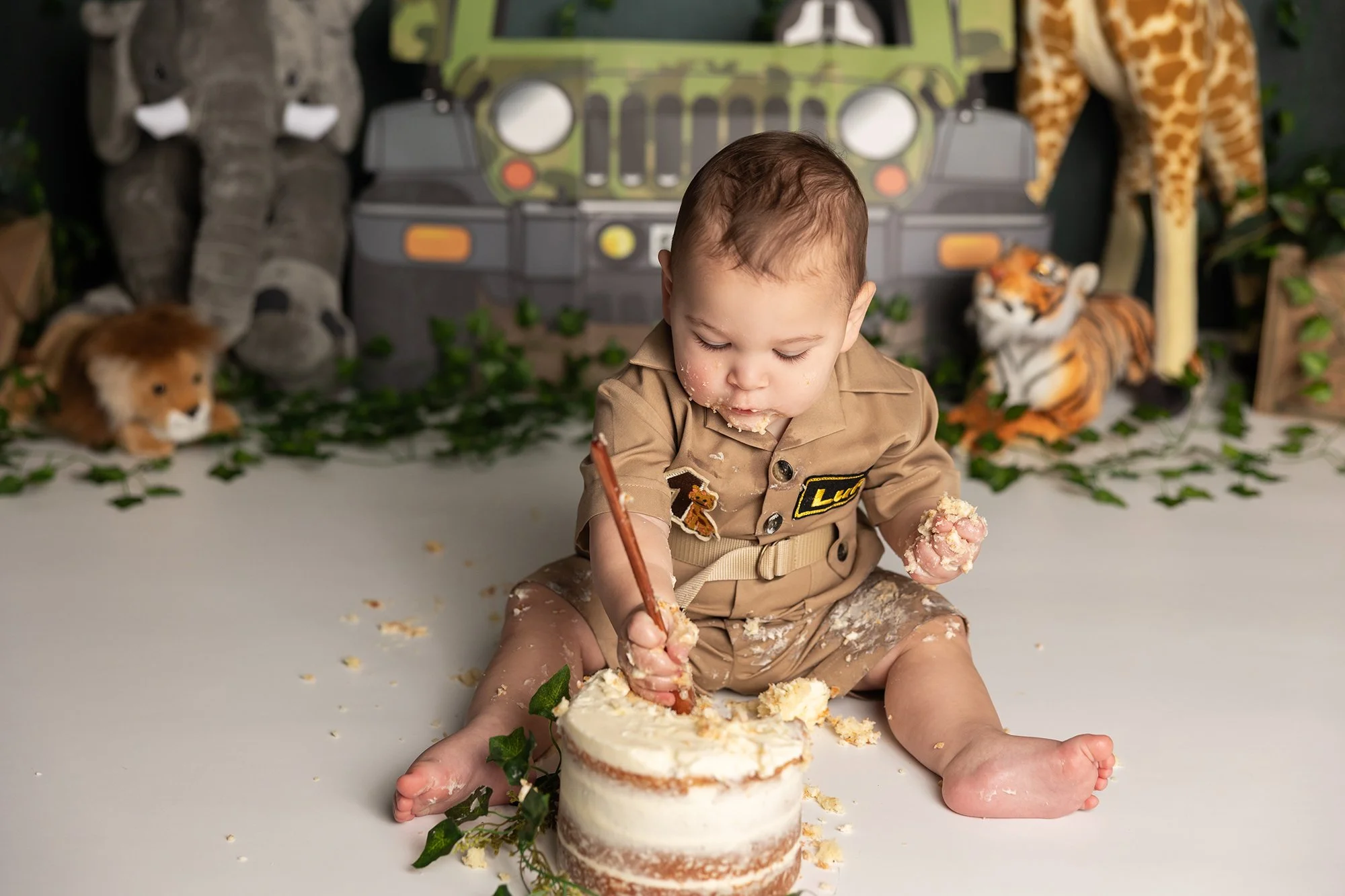 Baby boy smashing cake with a spoon during first birthday cakesmash session in Austin TX