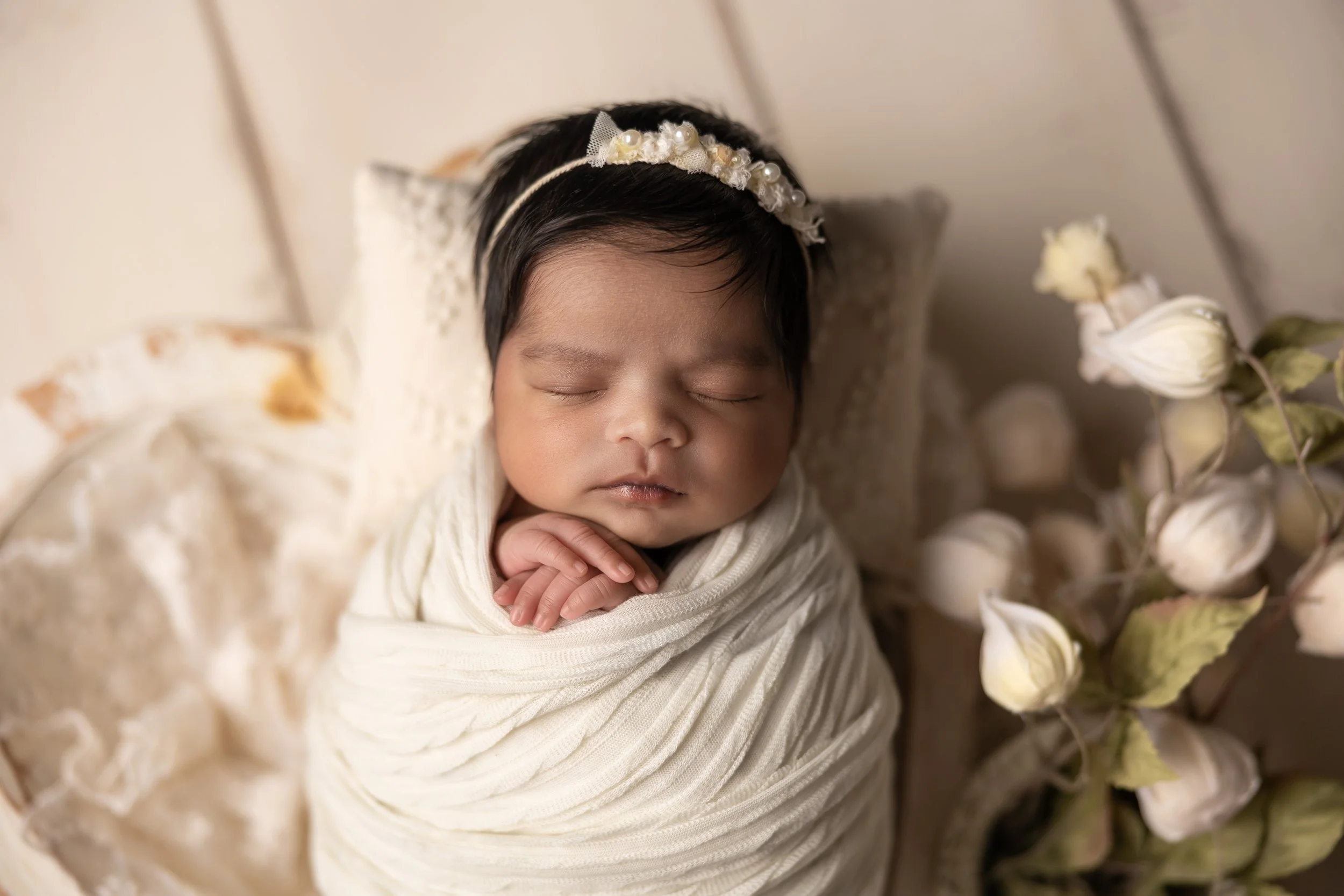 newborn baby girl swaddled in neutral tones with cream flowers