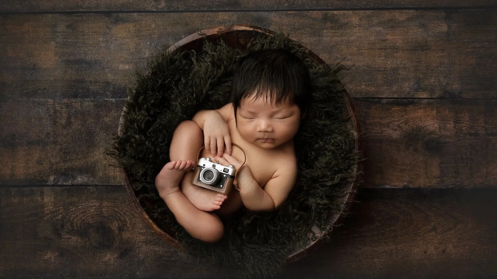 Sleeping newborn posed in a classic wooden bowl prop with a vintage camera, demonstrating a versatile newborn photography prop.