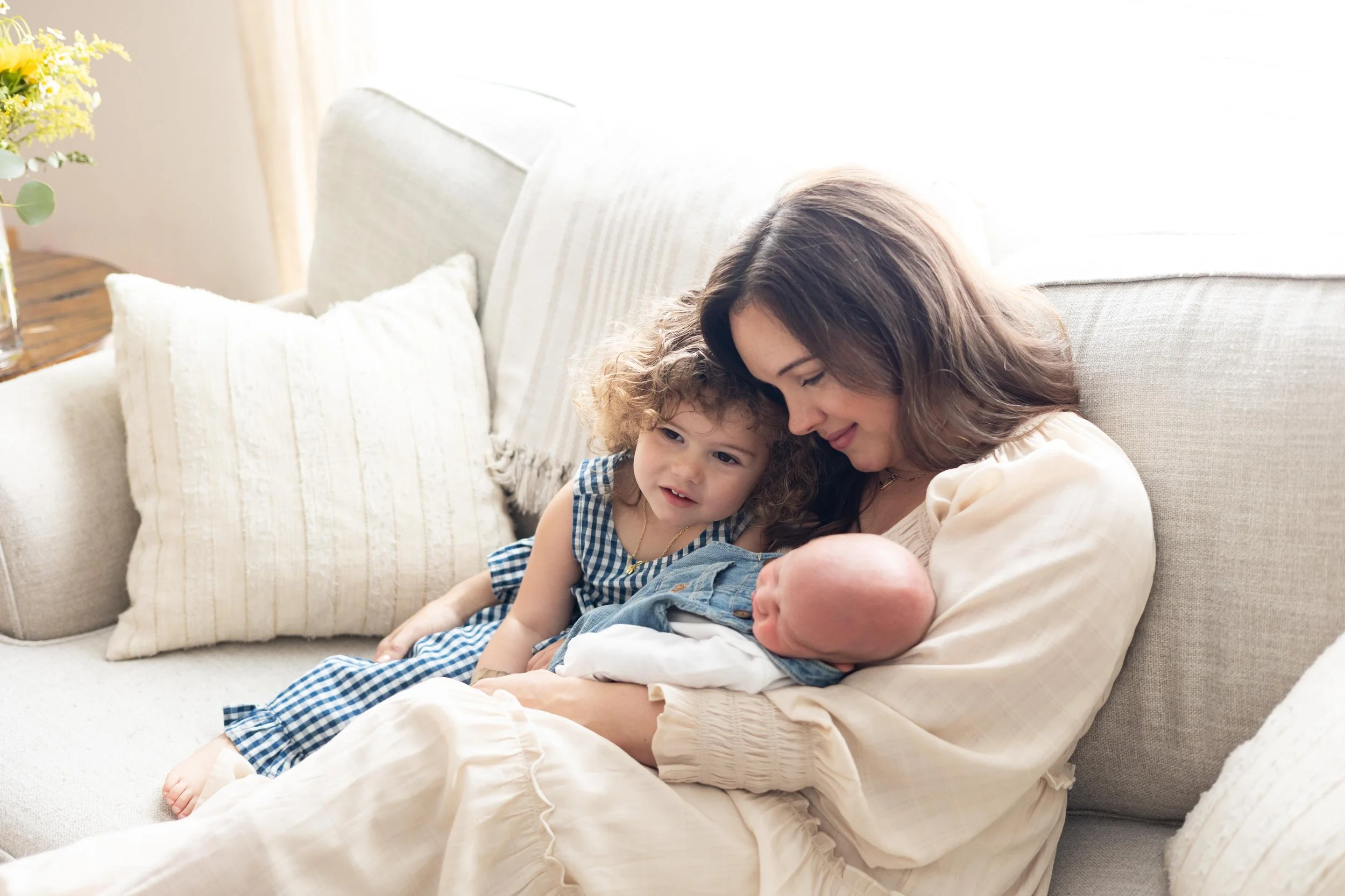 Mother holding newborn beside toddler during a relaxed lifestyle newborn session at home