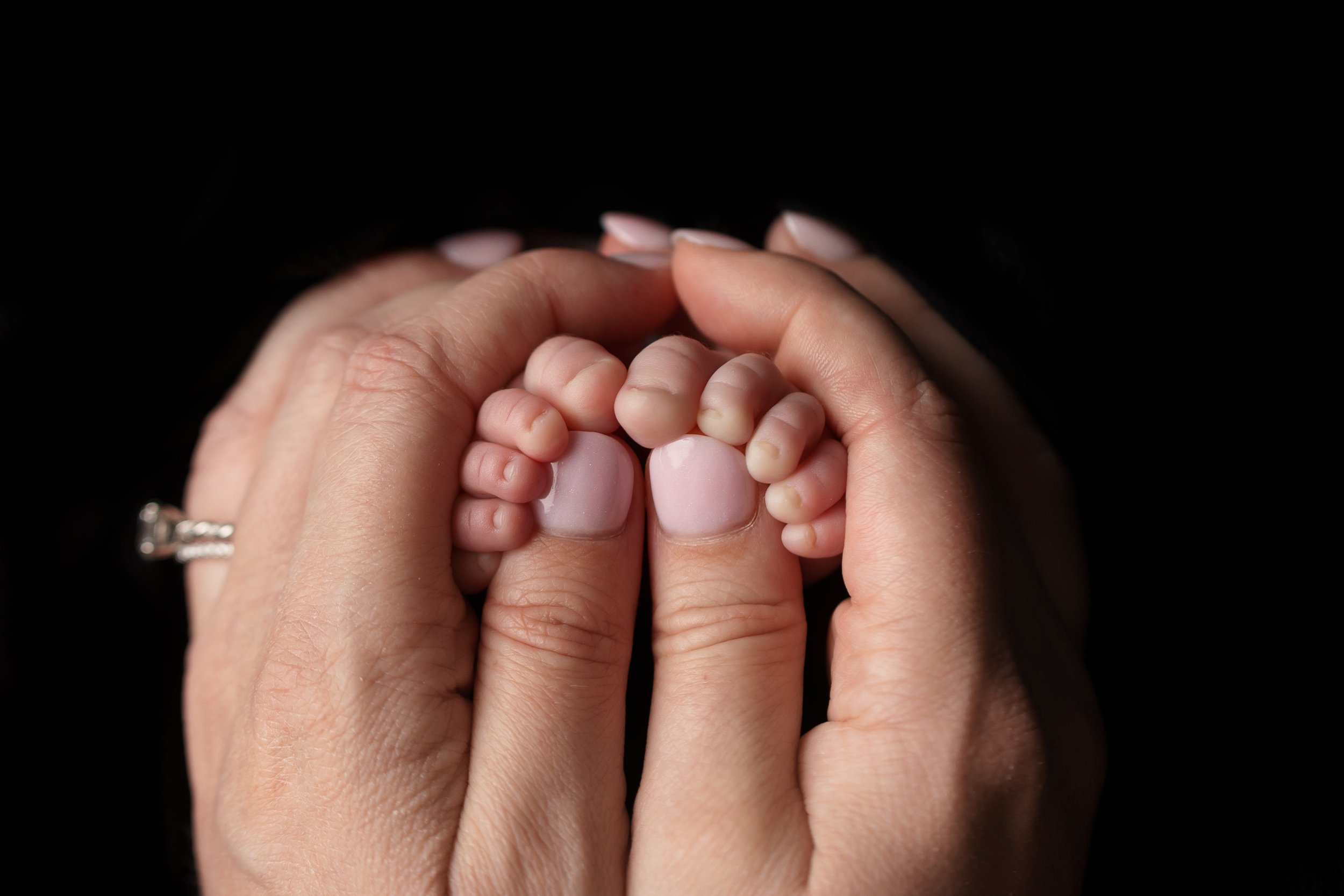 Close-up of a newborn's tiny hands wrapped around their mother's thumbs during a studio newborn session.
