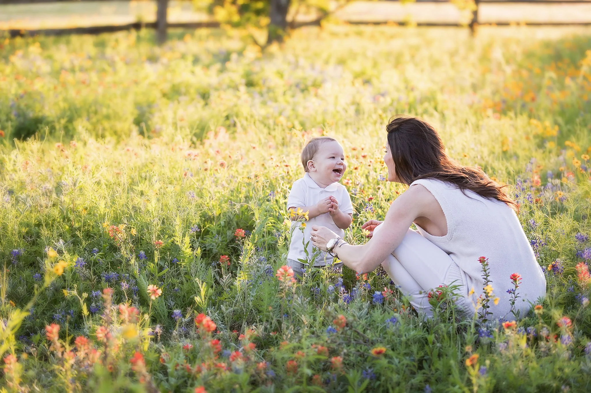 Mother laughing with her young son surrounded by bluebonnets and Indian paintbrush wildflowers during a spring photography session in Austin.