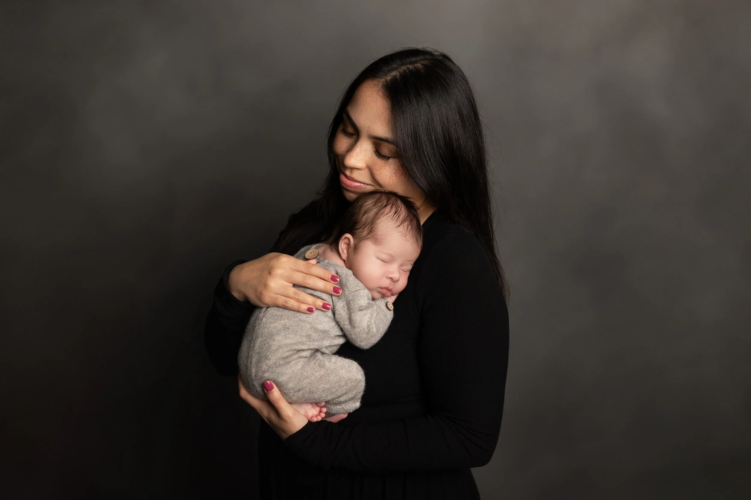 Mother cuddling sleeping newborn during a dark and moody studio portrait session